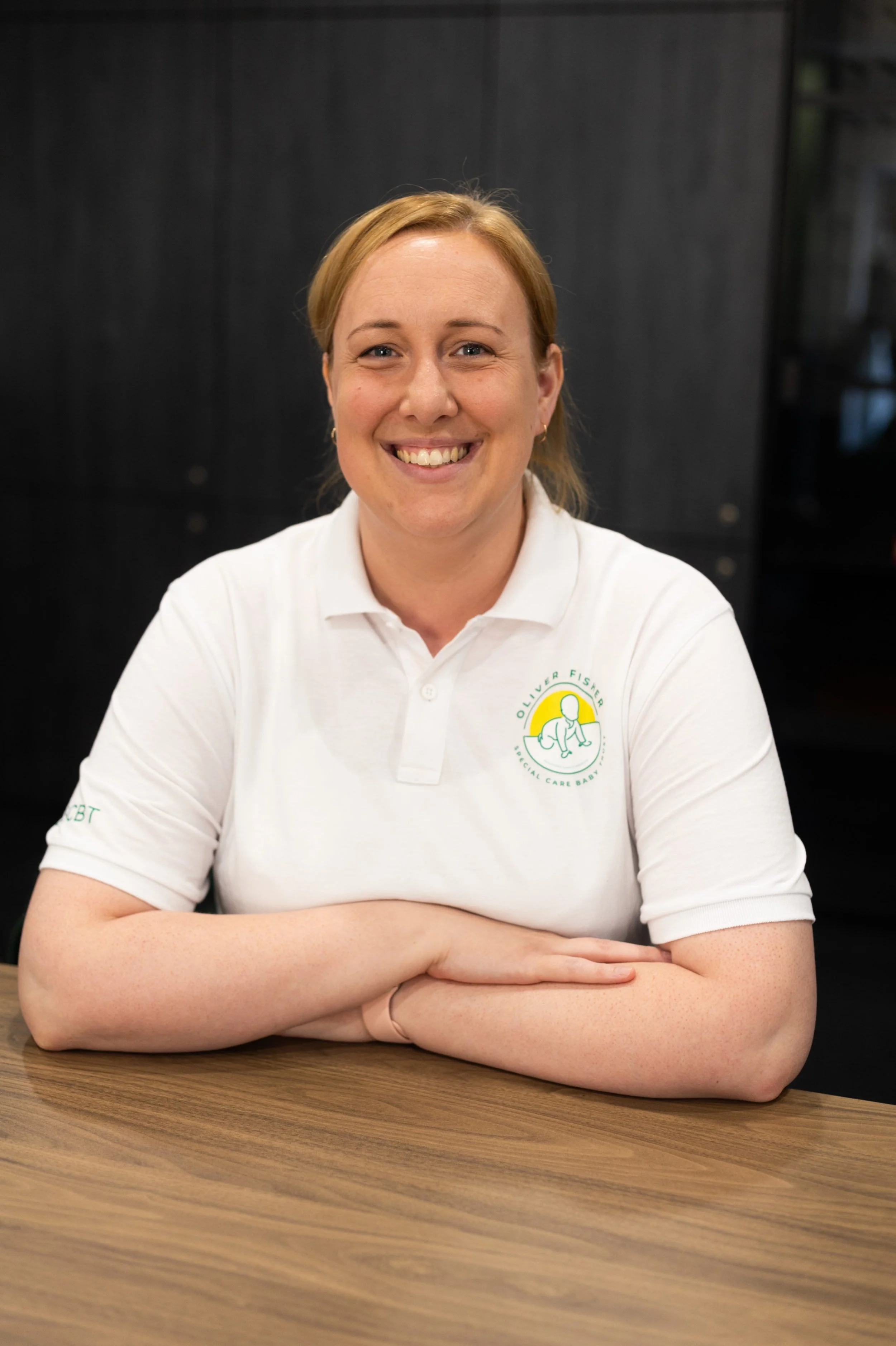 Woman smiling wearing white polo shirt with charity logo on plain background