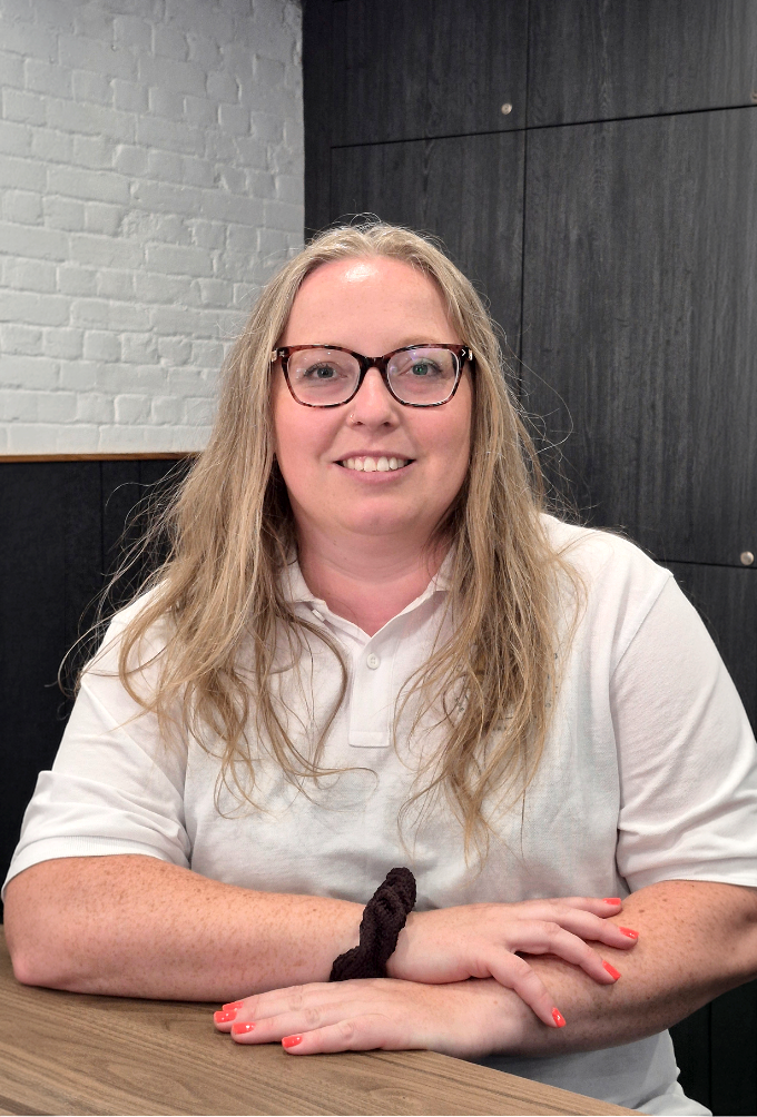 Woman smiling wearing white polo shirt with charity logo on plain background