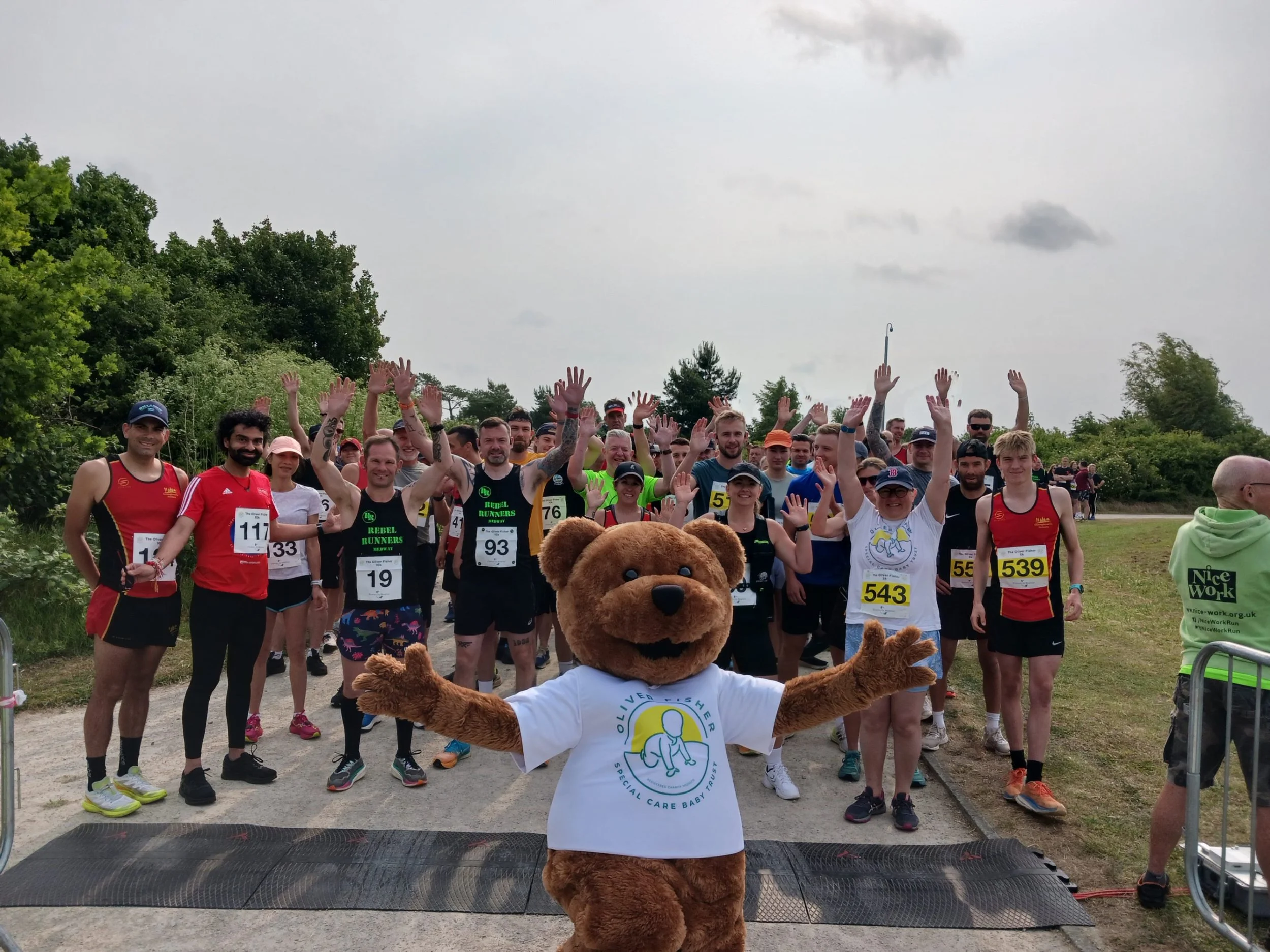 Large group of runners gathered outdoors with the charity bear mascot standing at the front of the crowd
