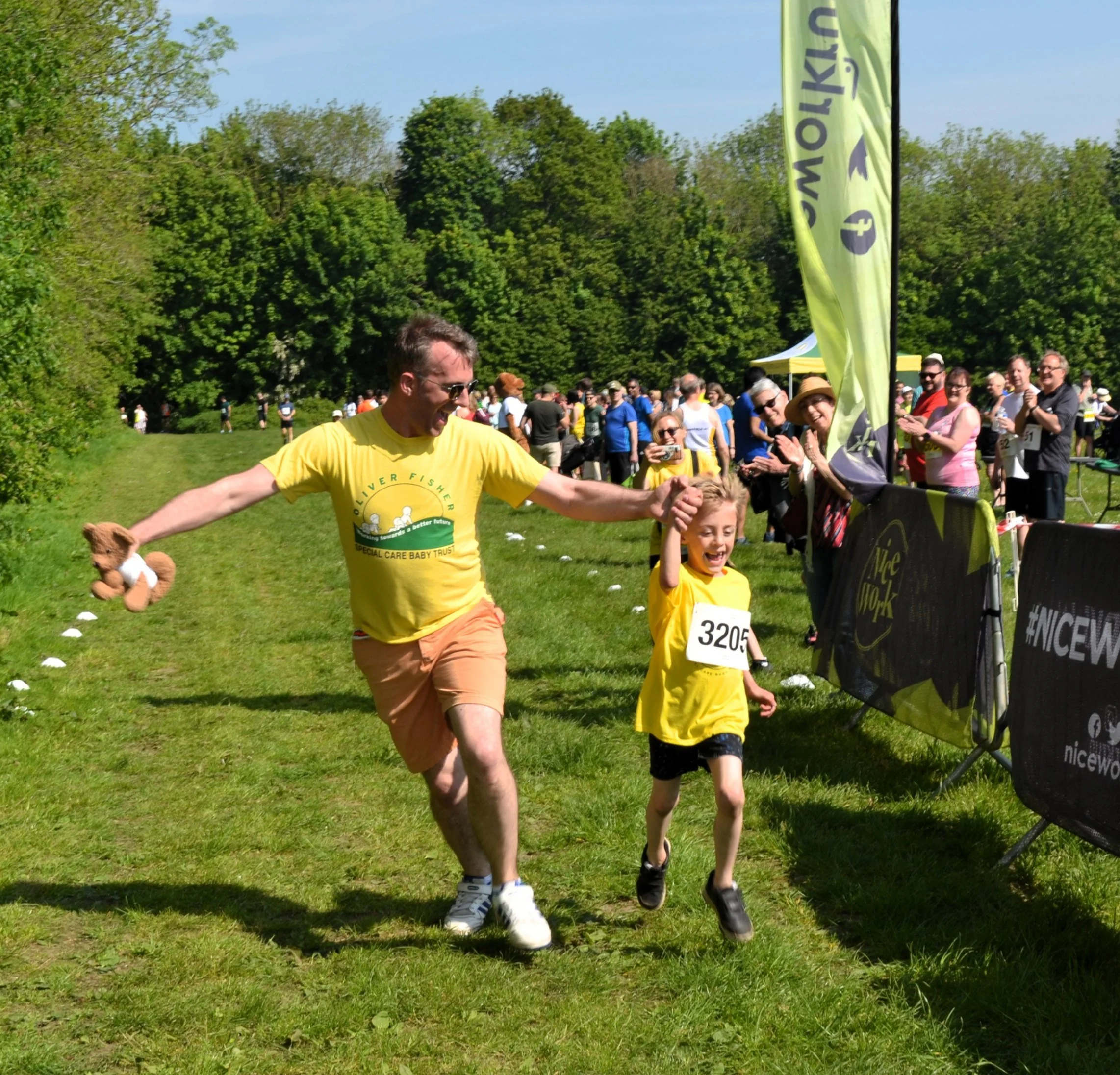 Adult and child crossing finish line together at charity run while spectators cheer
