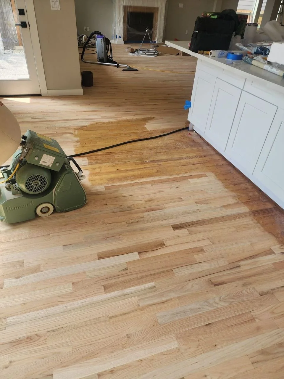 Wood flooring being sanded or refinished with a floor screw machine in a home interior.