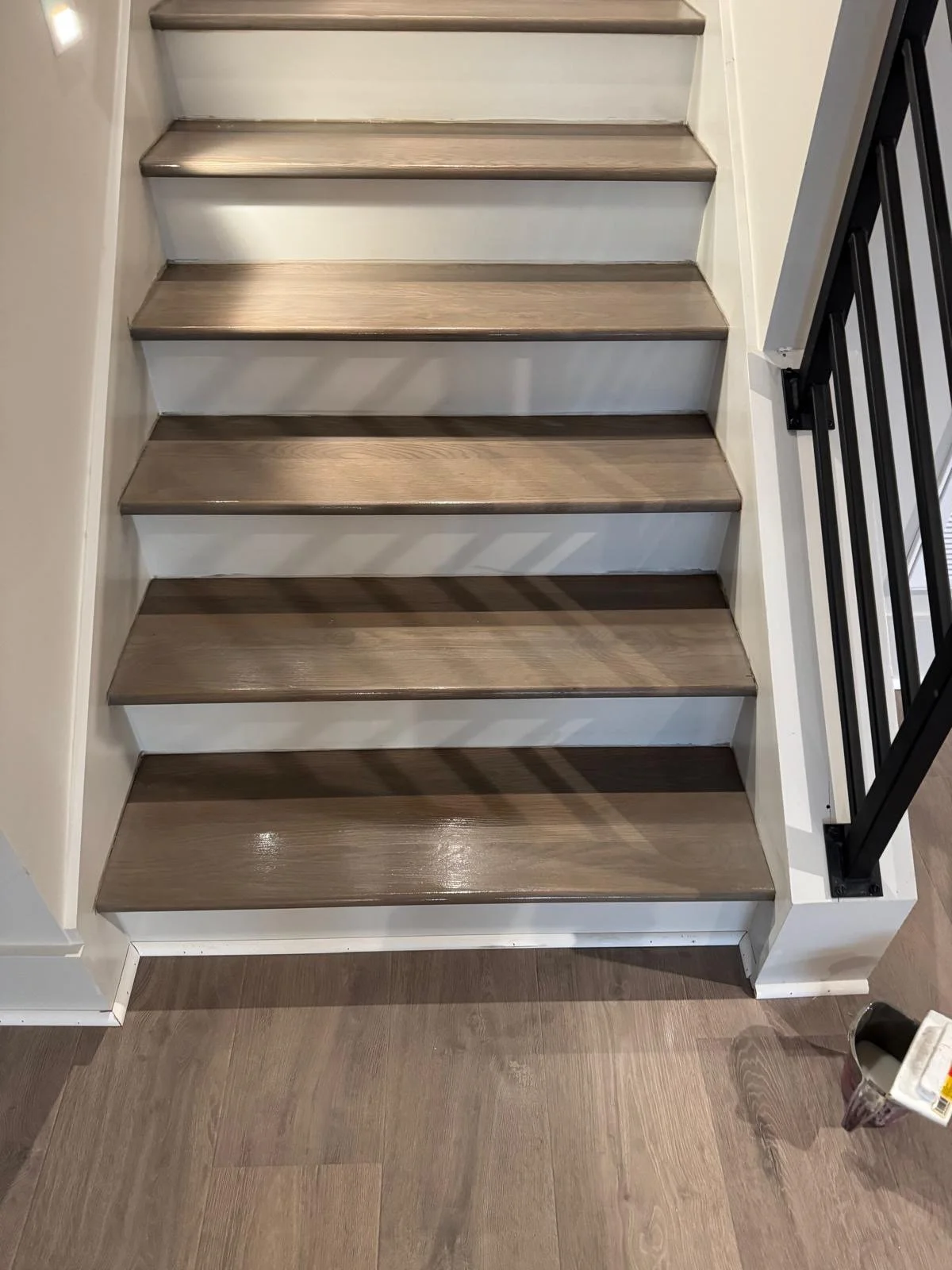 A staircase with six wood steps, each with a dark wood finish, and black metal railing on the right side.