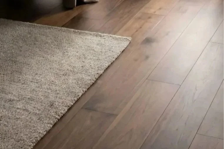 Corner of a room with a beige carpeted area and wooden flooring.
