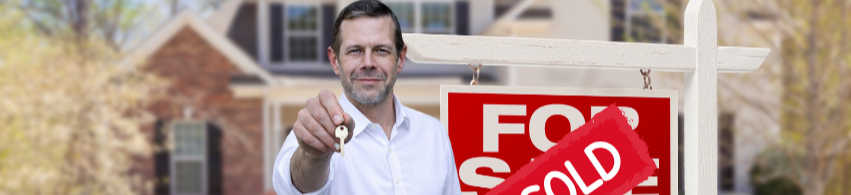 Man holding house key in front of a 'Sold' sign in front of a house.