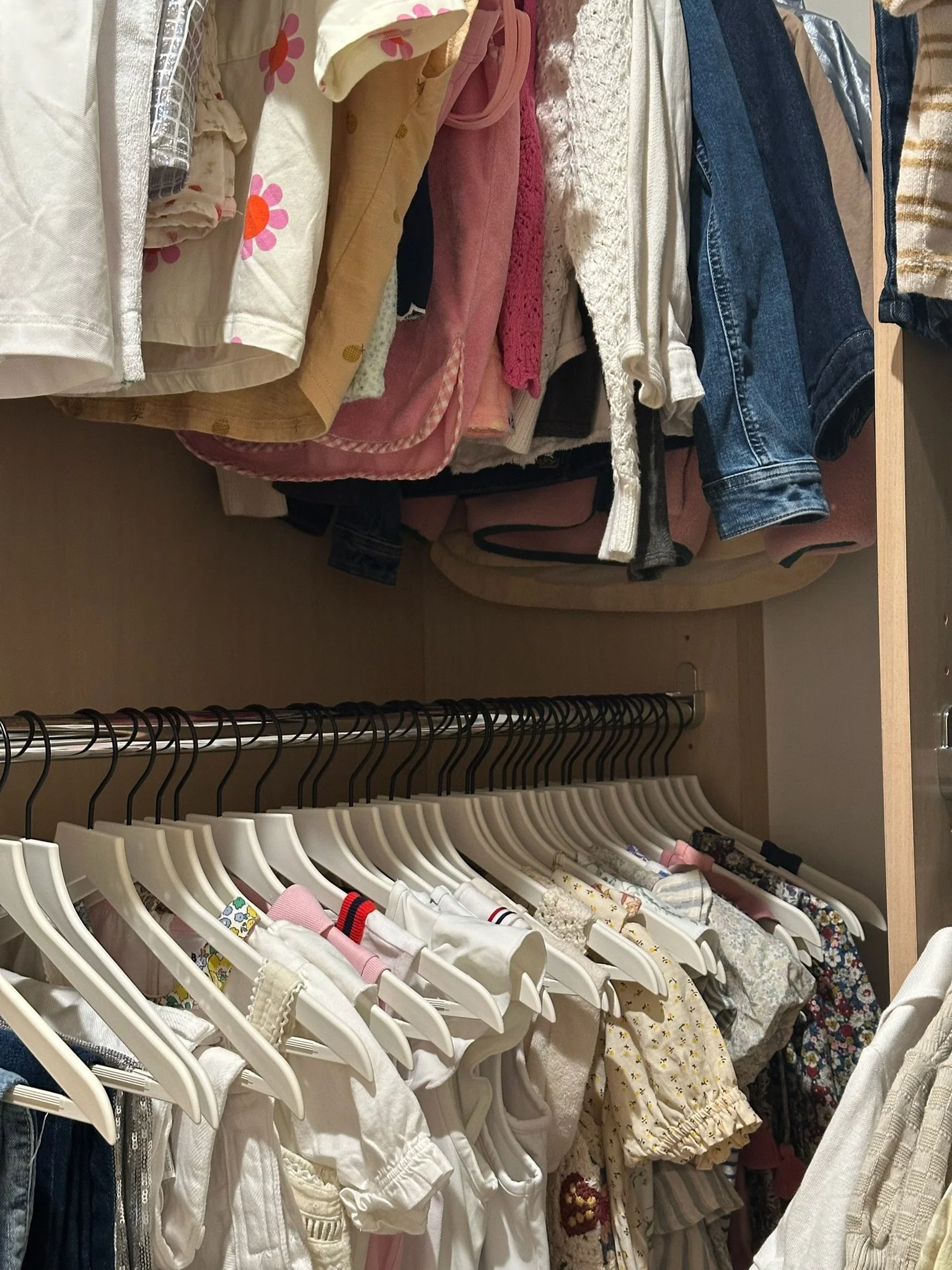 Children's clothing hanging in a closet, including dresses, shirts, and jackets.