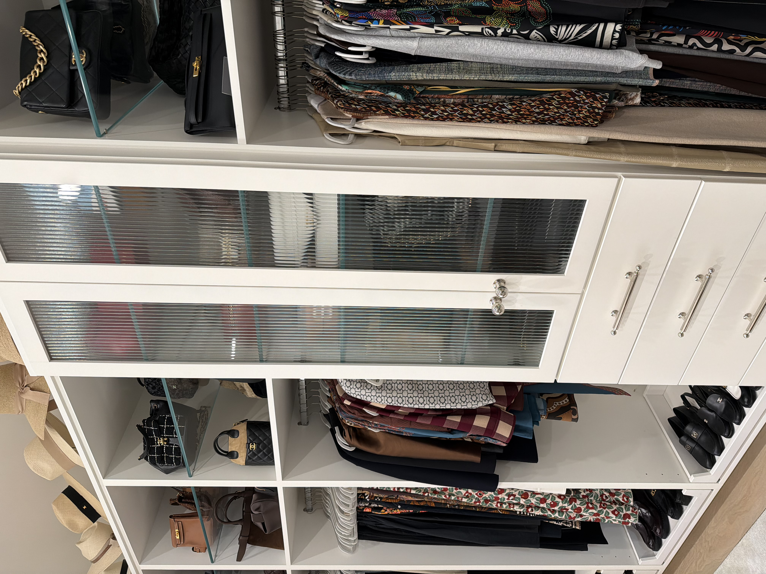 Closet with shelves of handbags, hats, folded clothes, and shoes.