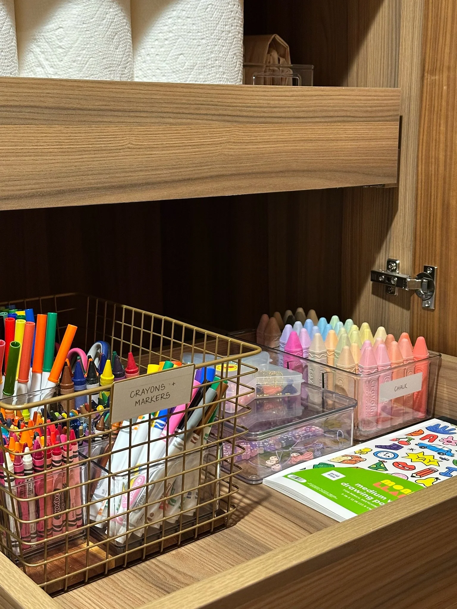 Open wooden drawer containing coloring supplies, including markers, crayons, chalk, and coloring books.