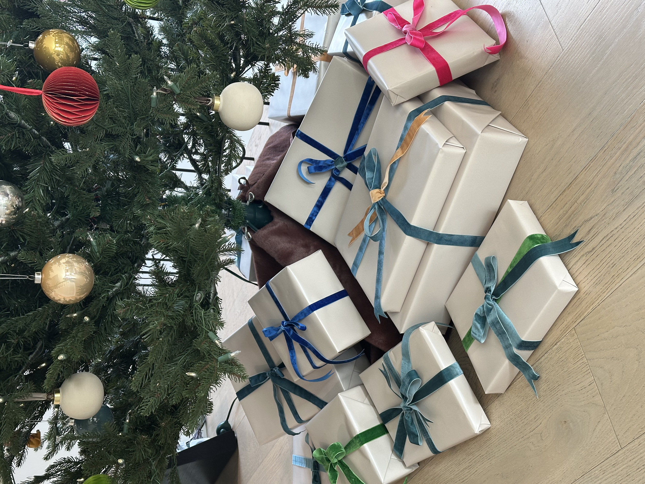Several wrapped Christmas presents with different colored ribbons under a decorated Christmas tree with ornaments.