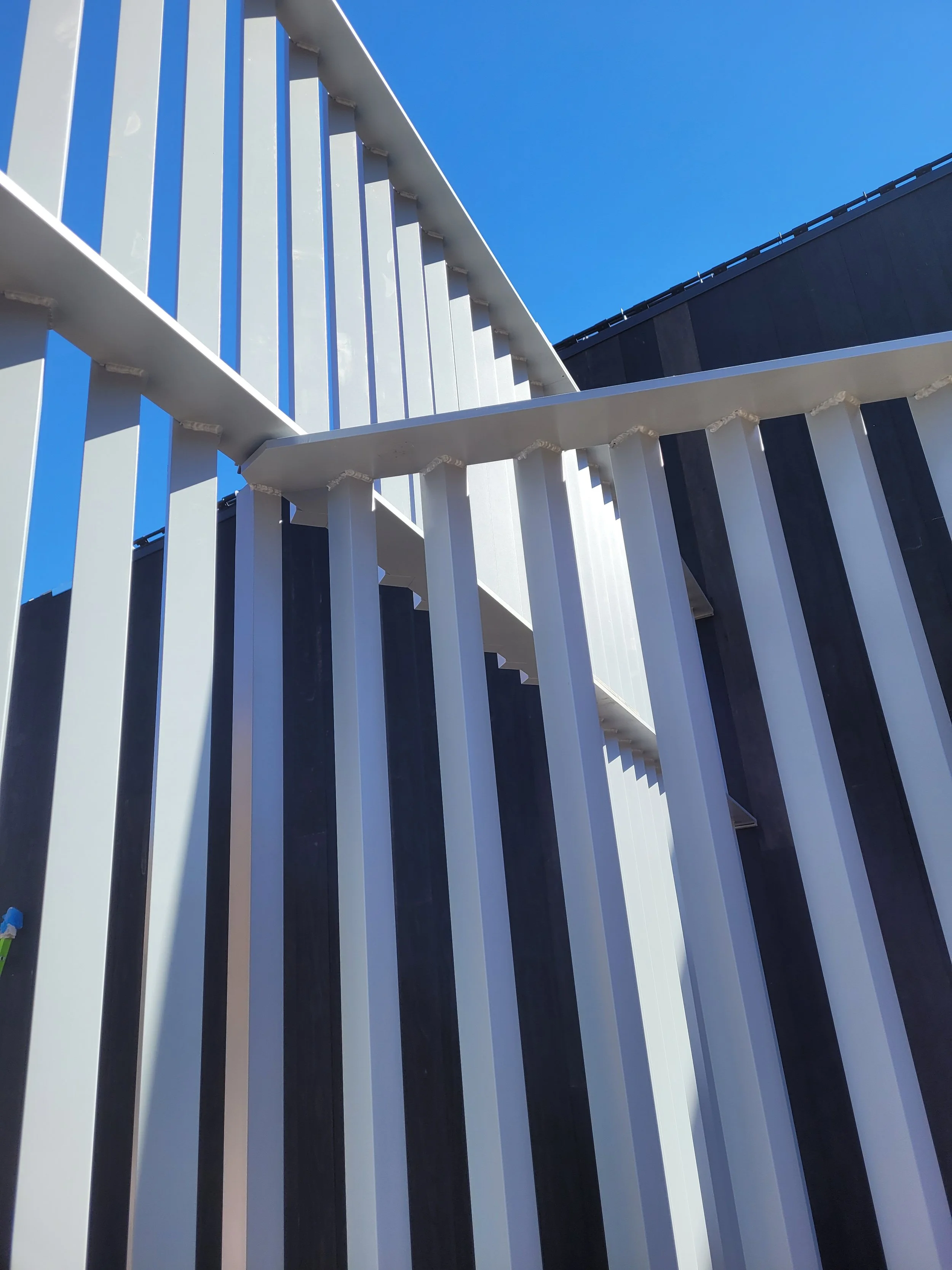 Close-up view of a modern black and white striped metal fence with vertical bars against a clear blue sky.