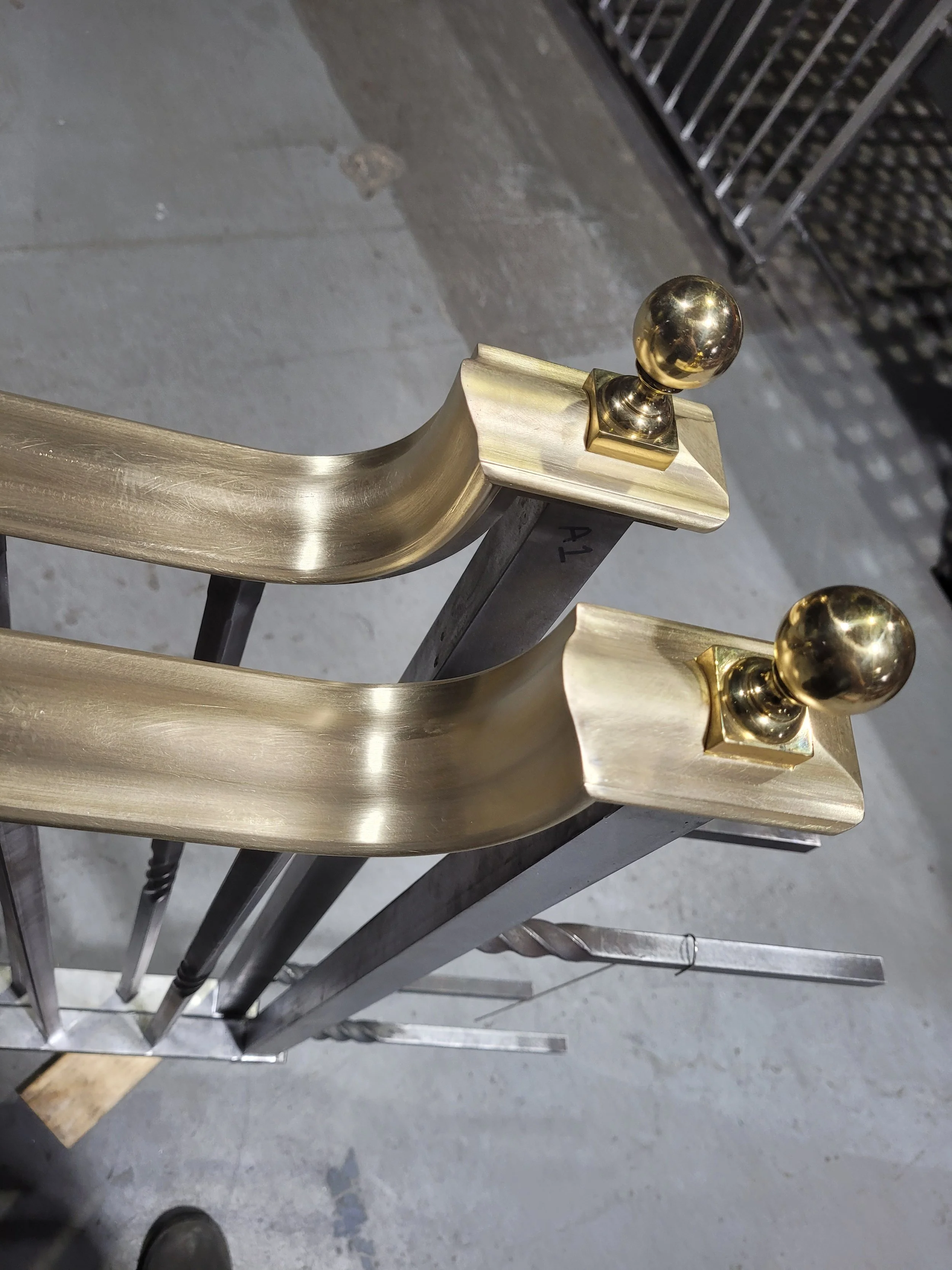 Close-up of two metal handrails with gold-colored decorative finials, mounted on a metal frame, in an industrial or storage area.