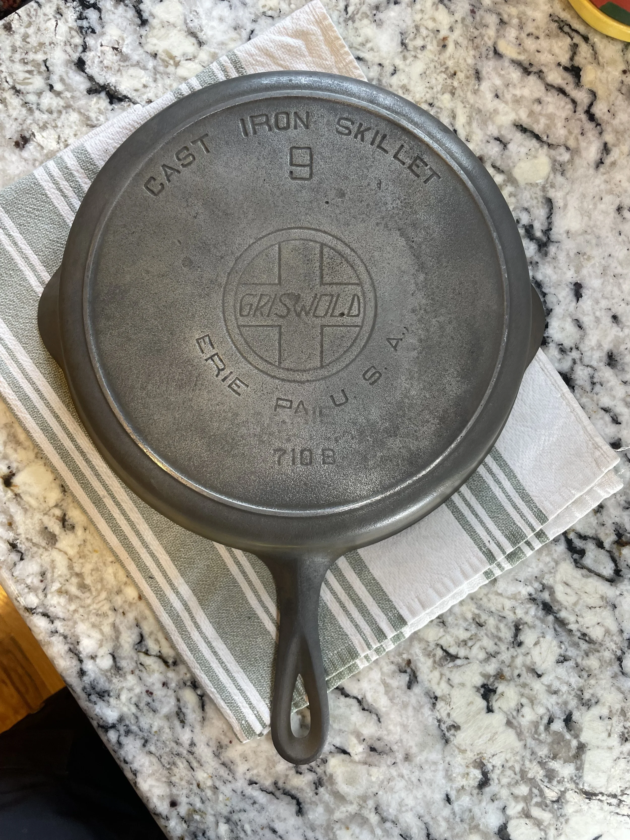 A Griswold cast iron skillet placed on a white and green striped cloth on a granite countertop.