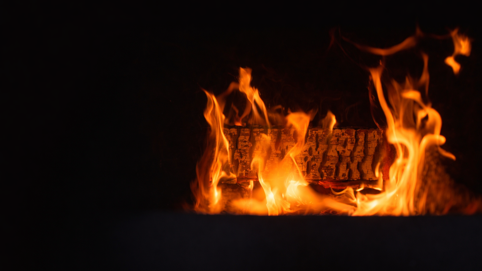 Fire burning with visible flames and charred wood in a dark environment.
