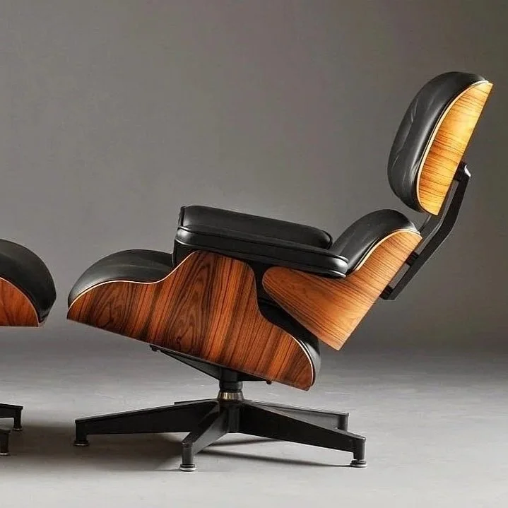 A modern lounge chair with a matching ottoman, featuring wooden accents and black leather upholstery, set against a plain grey background.