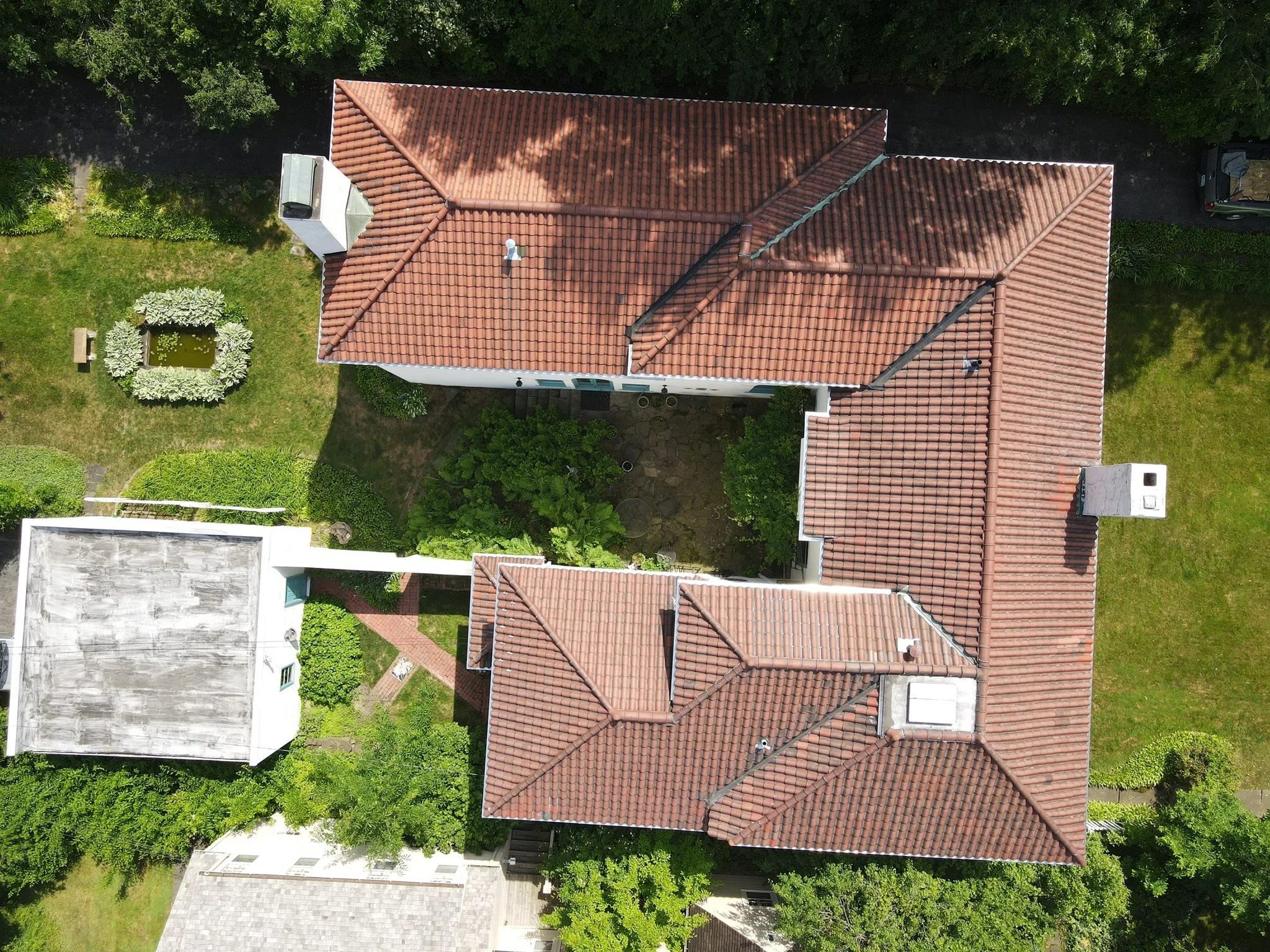 Aerial view of a house with red tile roof, surrounded by green garden and trees, with neighboring houses nearby.