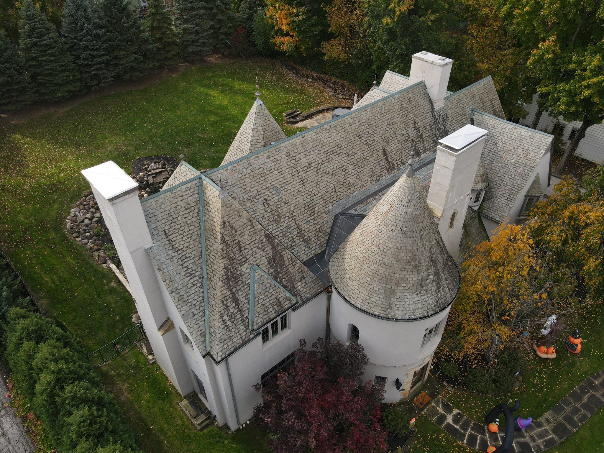 Aerial view of a Victorian-style house with a steep roof, turrets, and multiple chimneys, surrounded by a lawn and trees