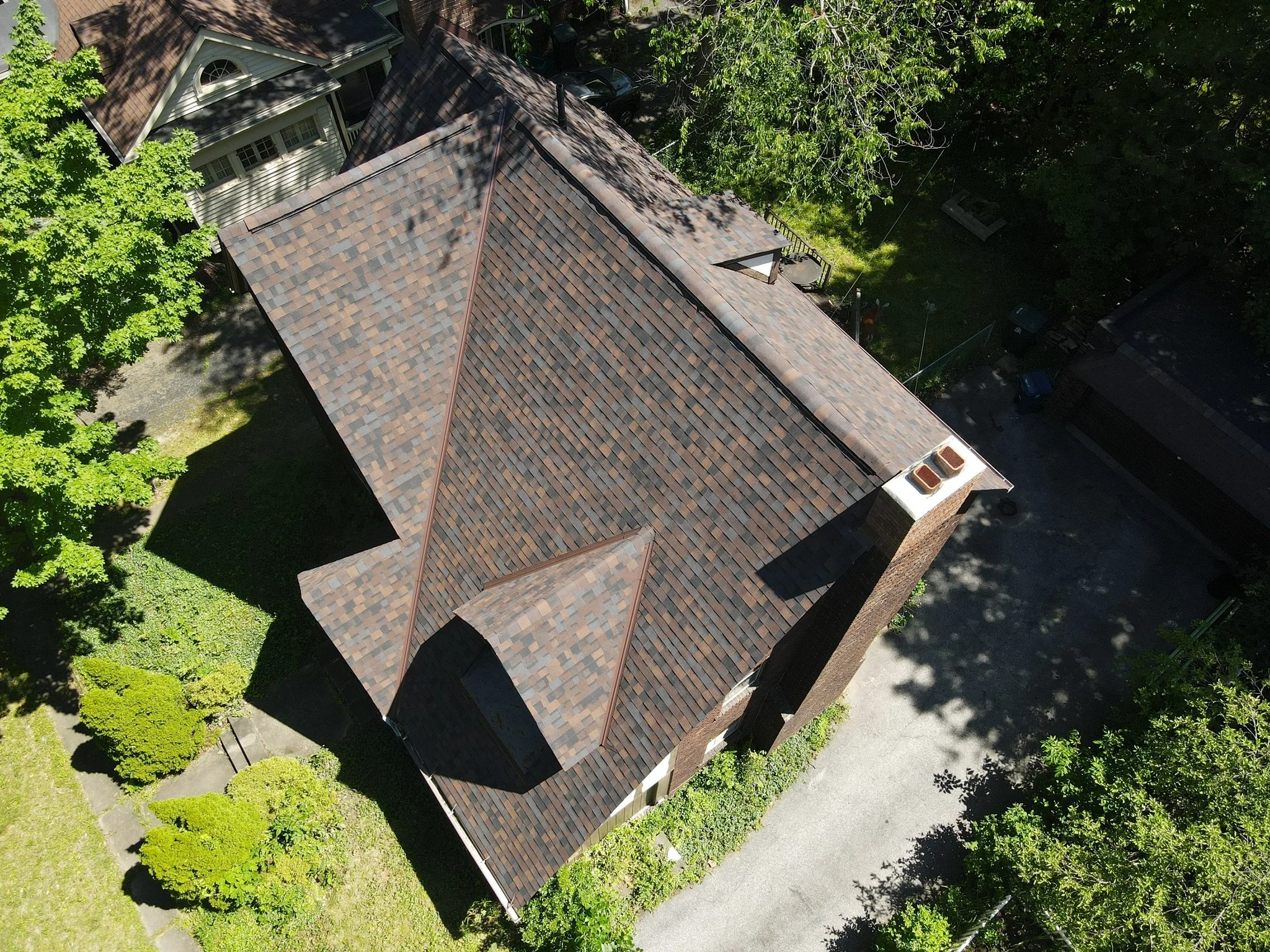 Aerial view of a house with a complex shingle roof, surrounded by trees and a small driveway.