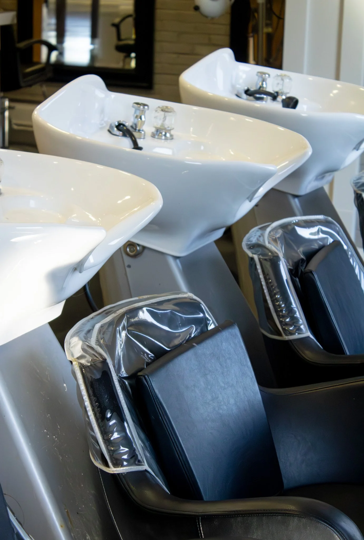 Hair washing stations with white sinks and black chairs in a salon.