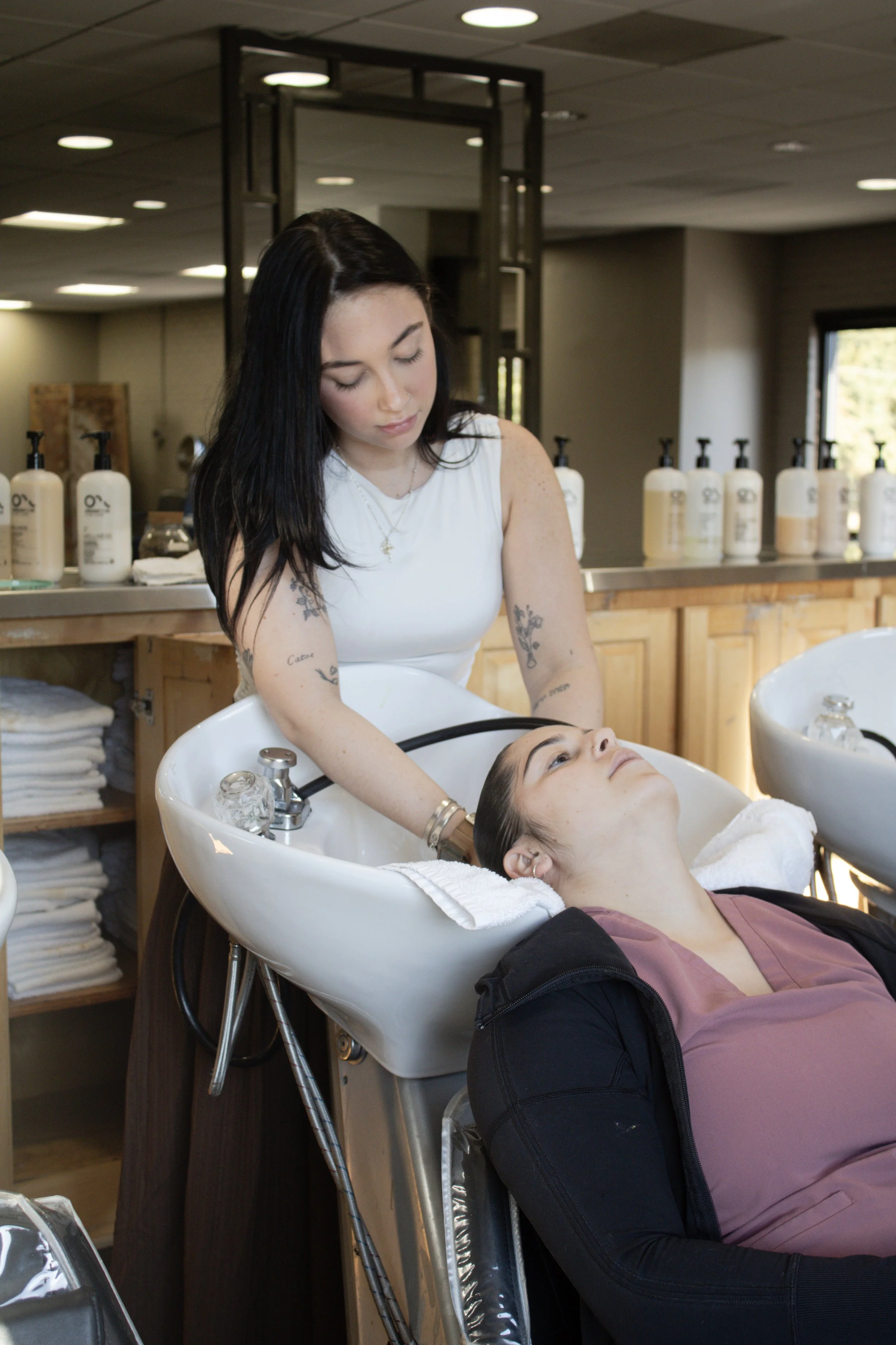 A woman receiving a hair wash at a salon with hair washing stations in the background.