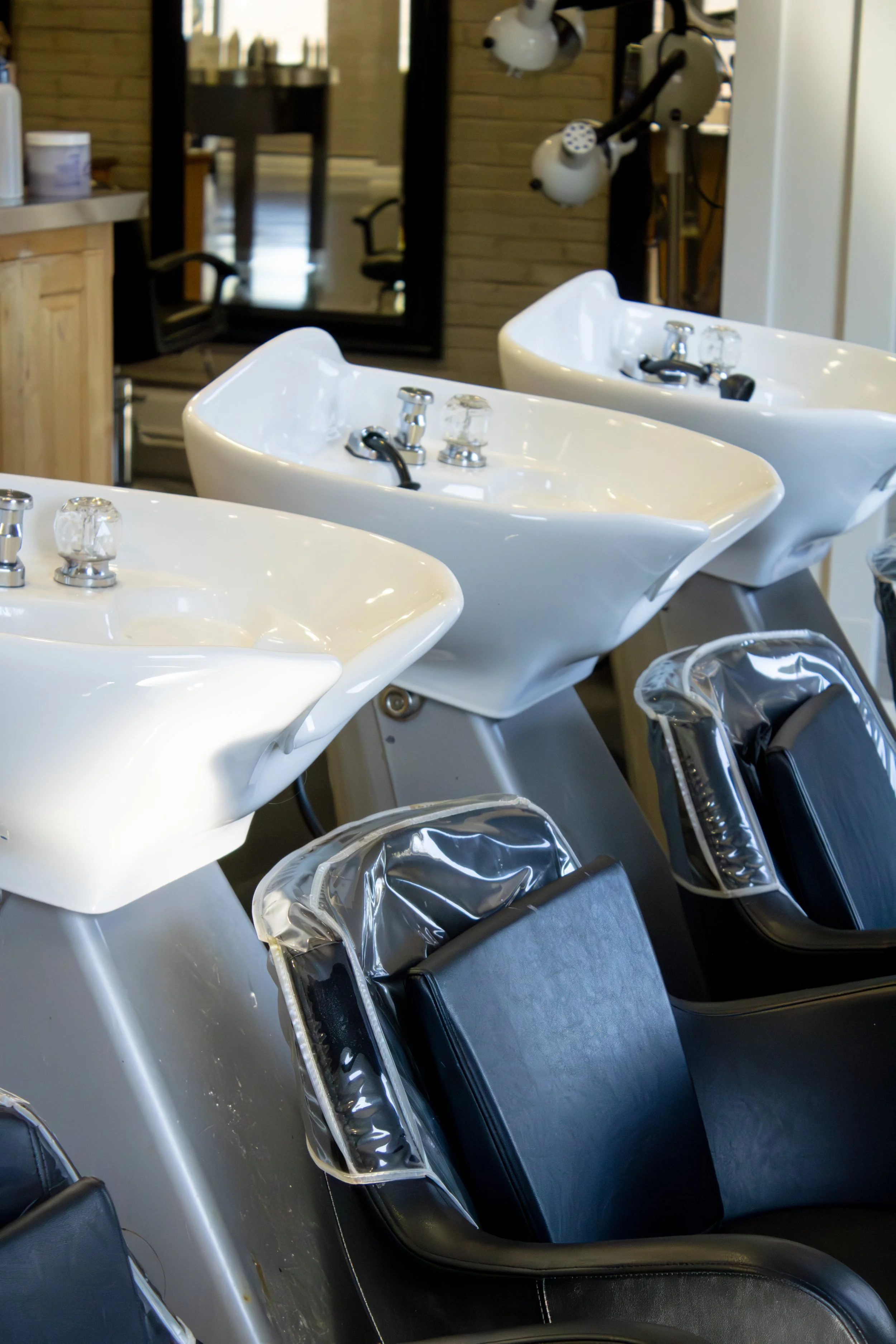 Three salon shampoo bowls with black chairs in front of them, set in a hair salon or barbershop.