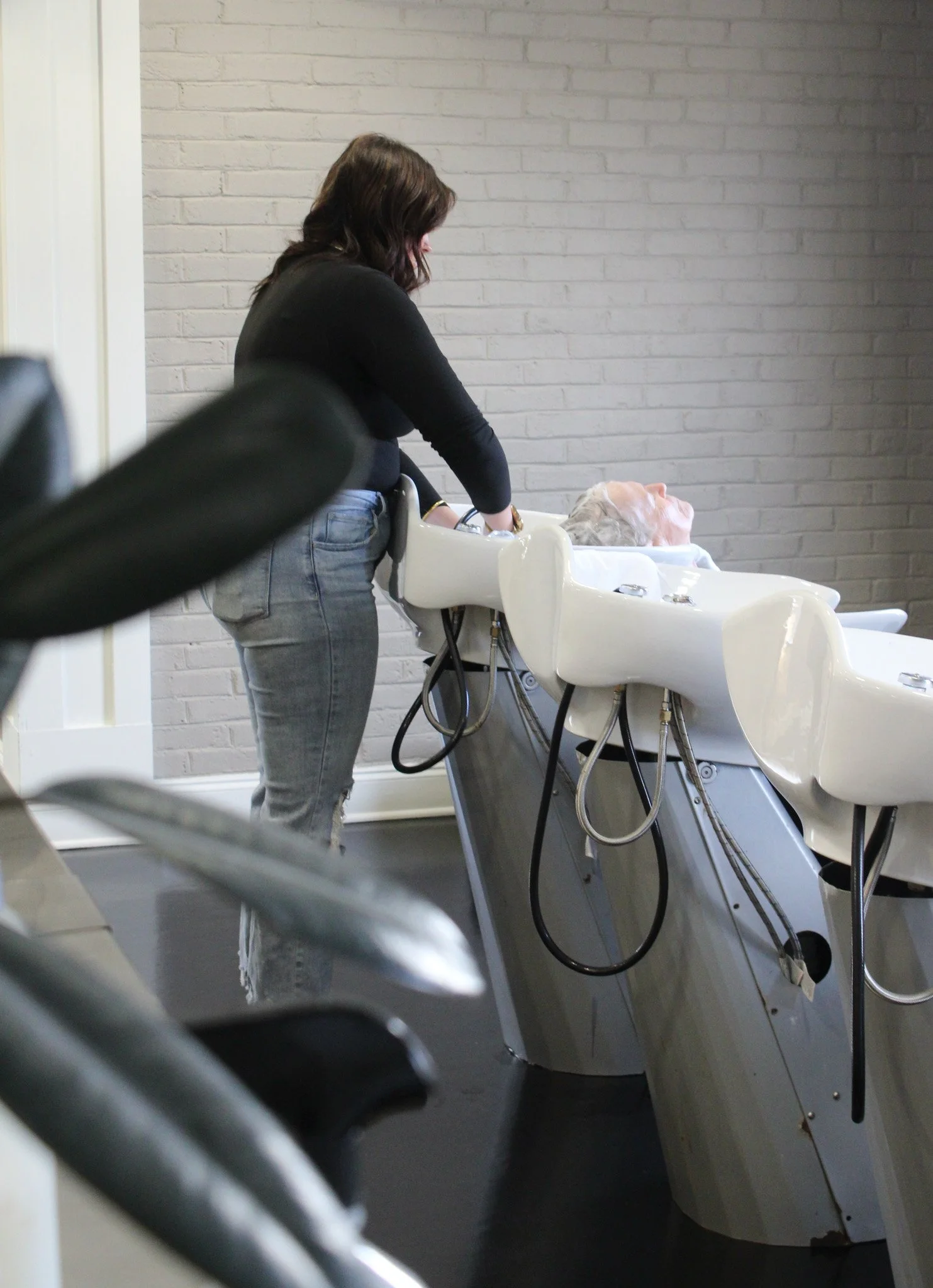 A woman washing a senior person's hair in a salon shampoo station.