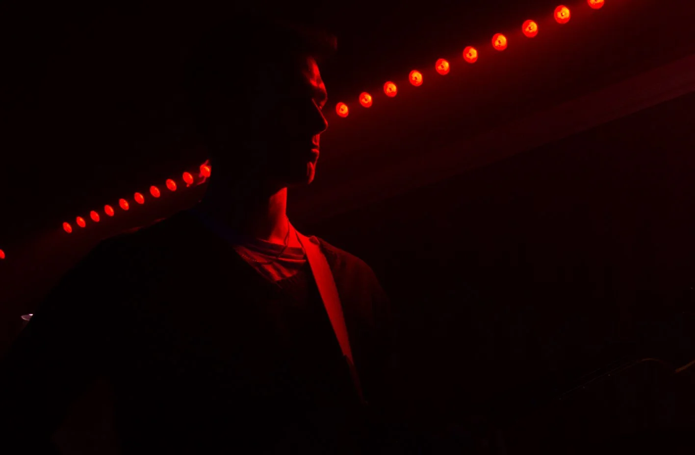 Person playing guitar in dark room illuminated by red LED lights.