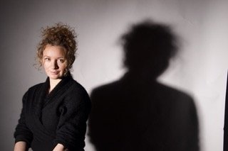 Woman with curly hair standing next to a wall casting a shadow
