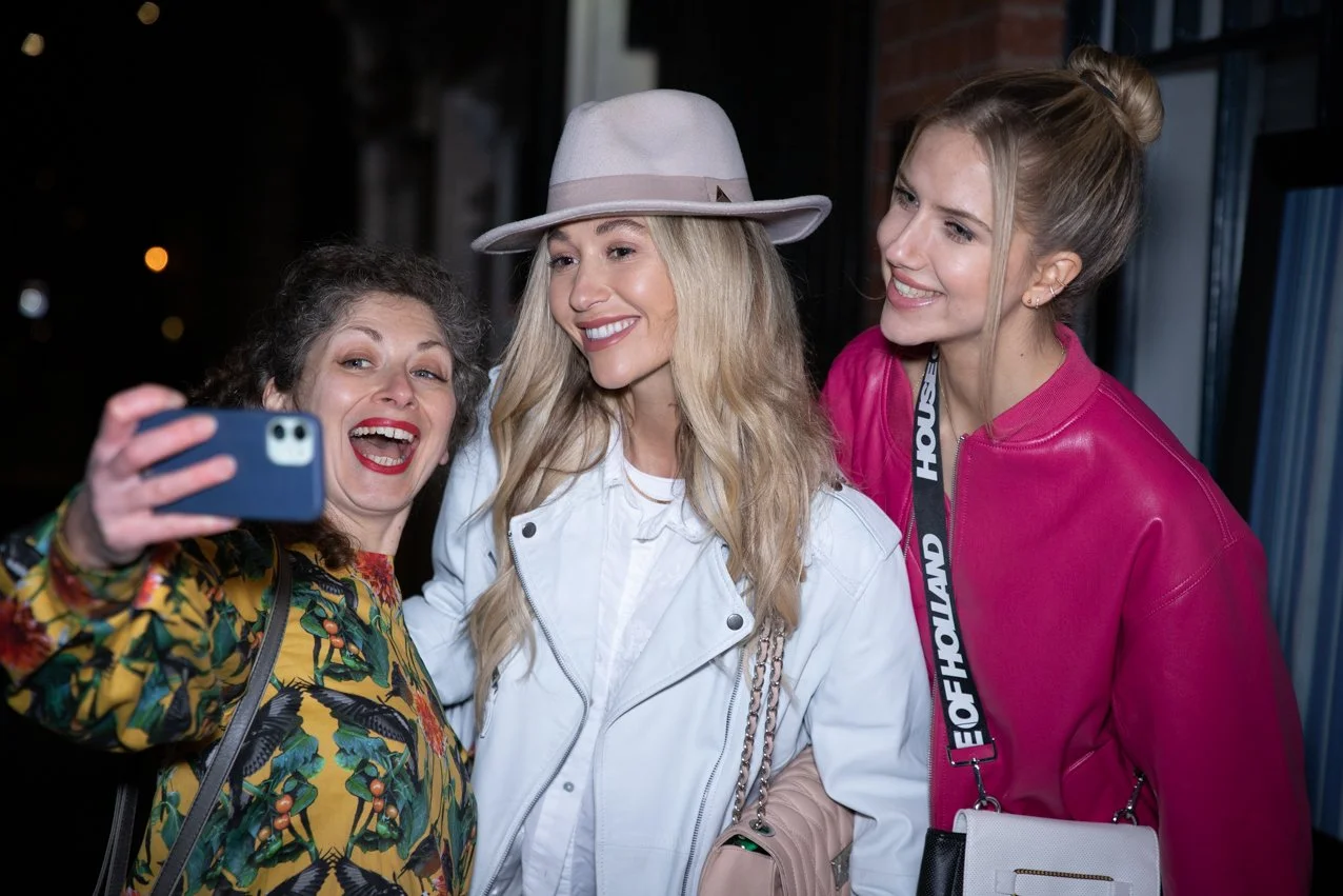 Three women taking a selfie together at night, smiling and posing for the camera.