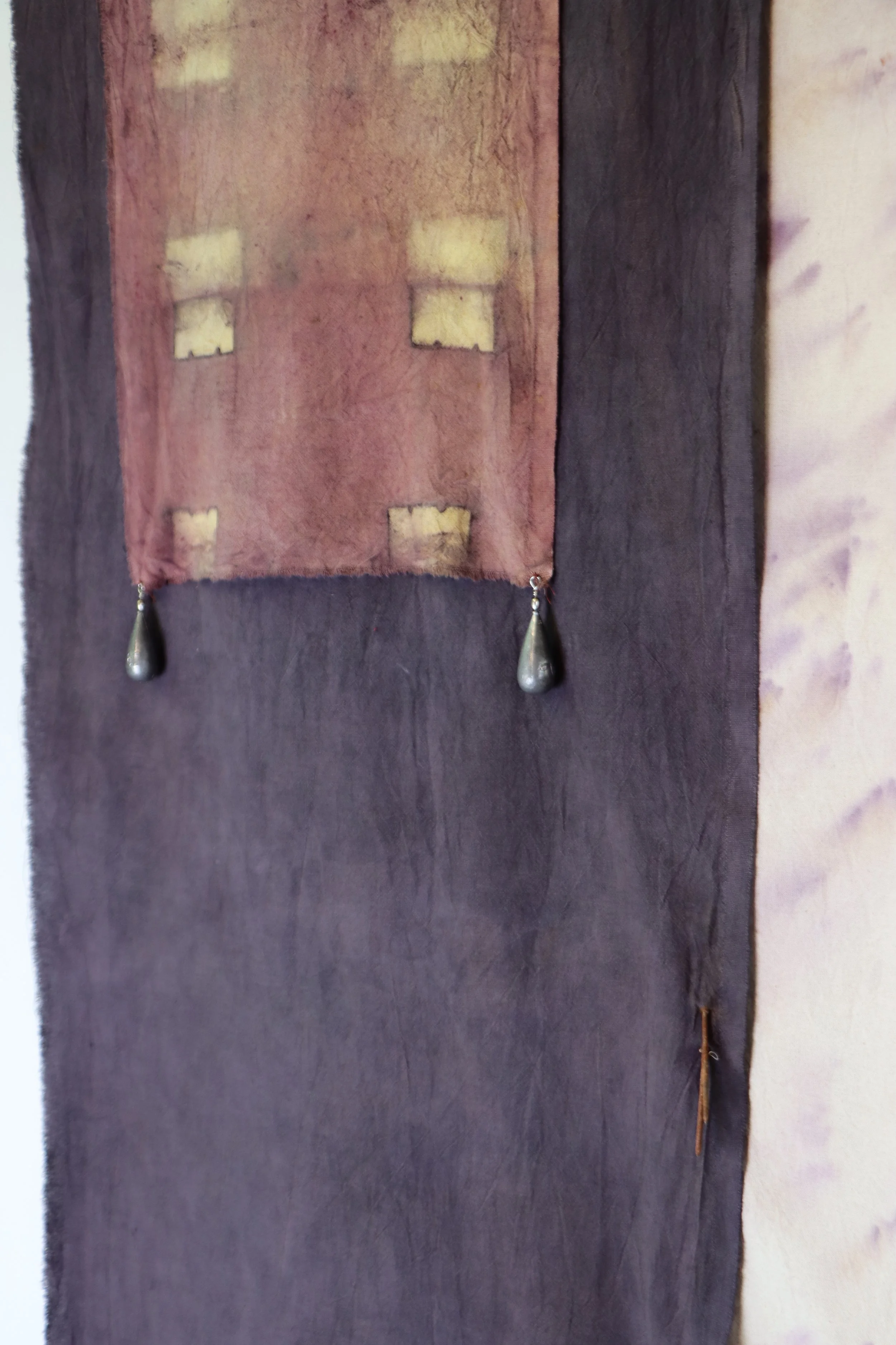 Decorative fabric wall hanging with small window patterns and attached teardrop-shaped earrings.