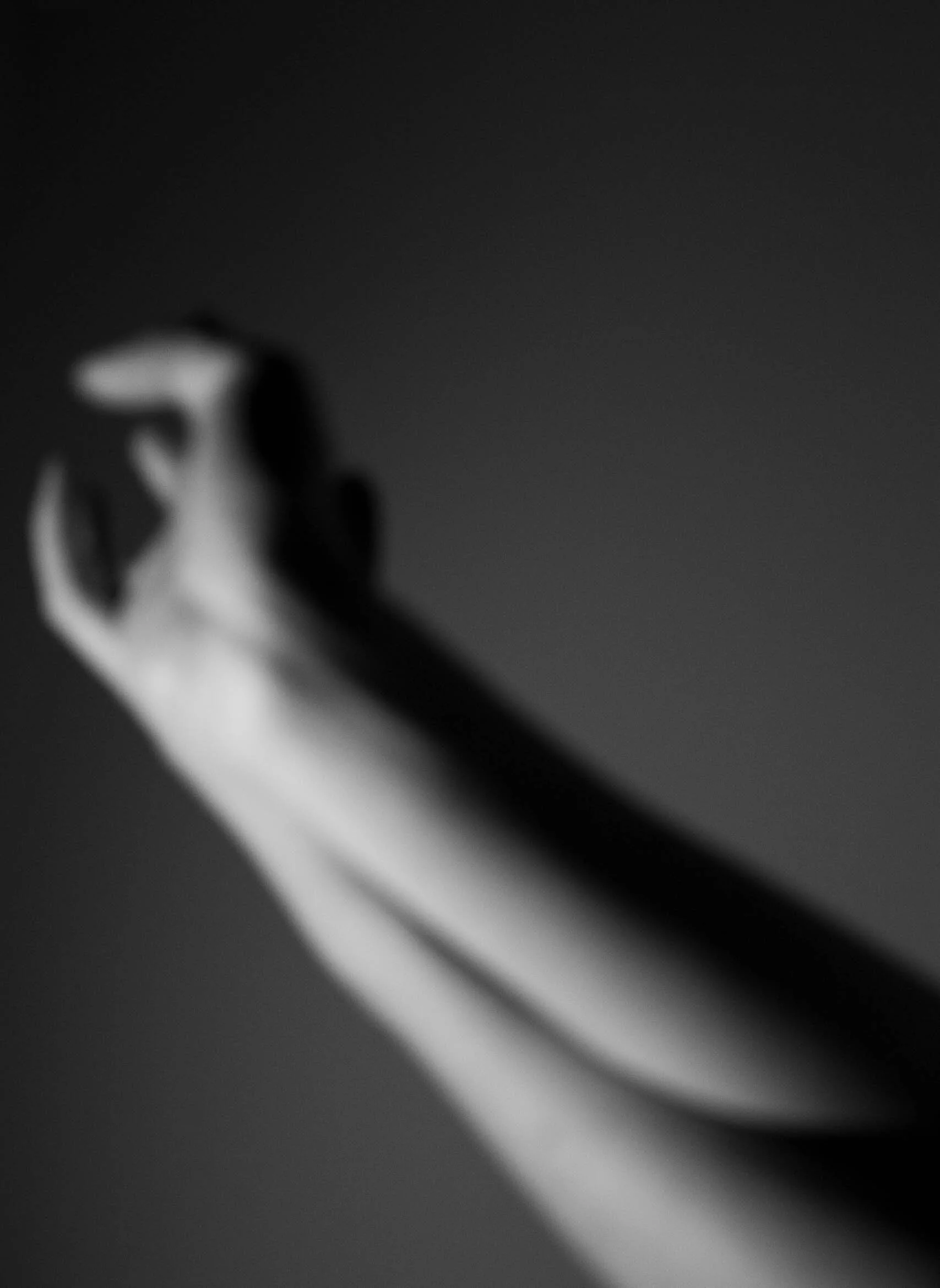 Blurred black and white image of a hand with fingers crossed, with no specific background details visible.