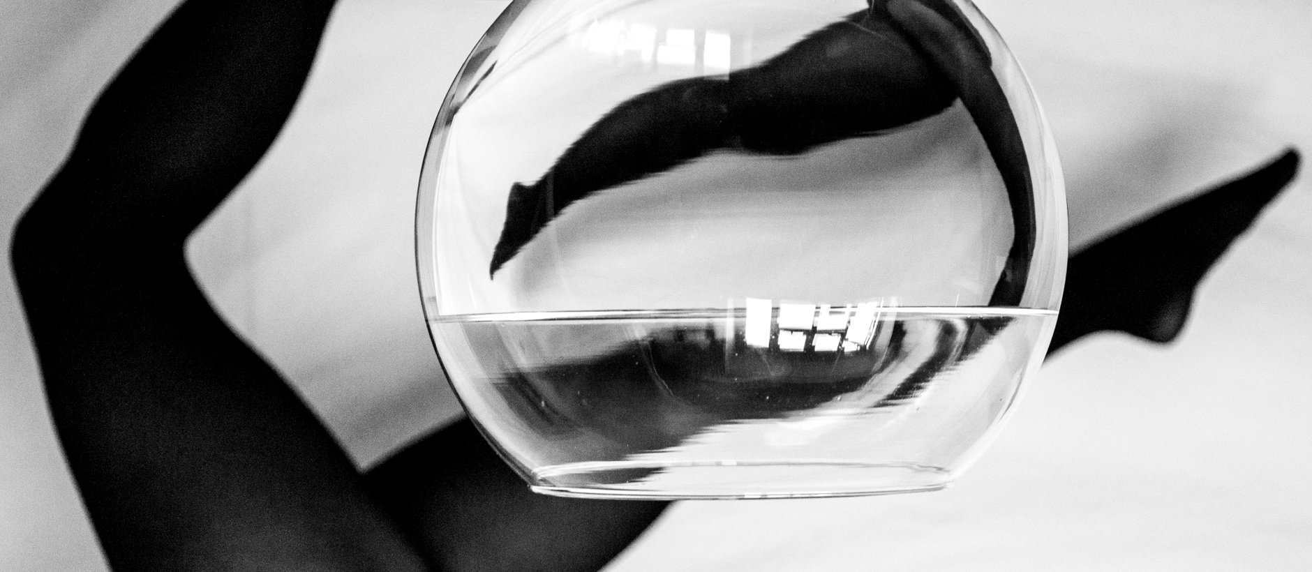 A hand wearing a black glove holding a glass of water with a dark cloth inside, creating a visual distortion.