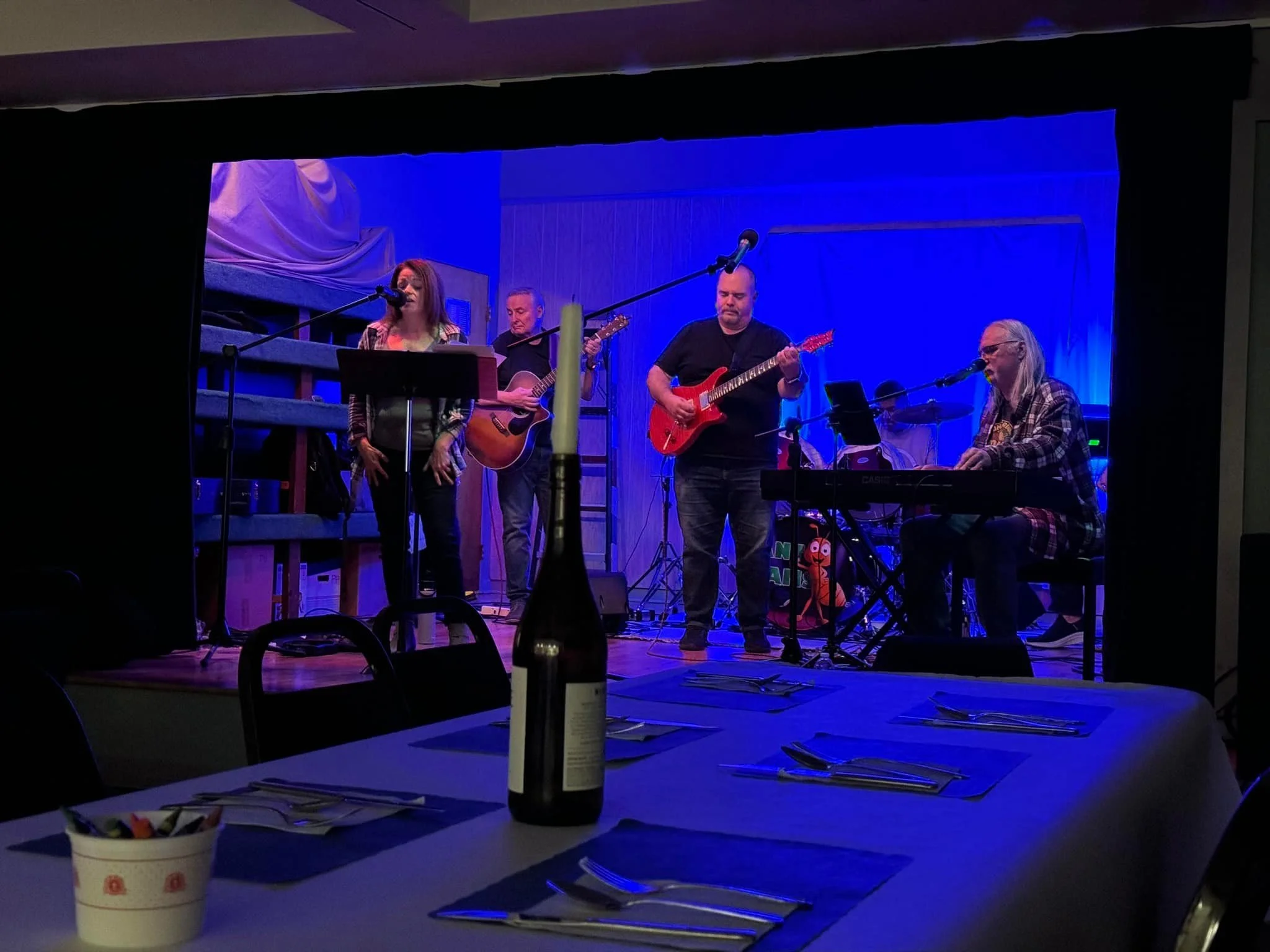 A band performing live on stage with three guitarists and a keyboard player, under blue stage lighting.