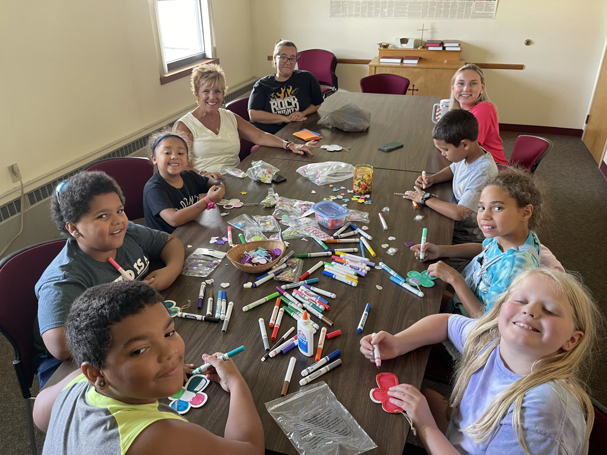 Children and adults sitting around a table with arts and crafts supplies, smiling and making colorful decorations.
