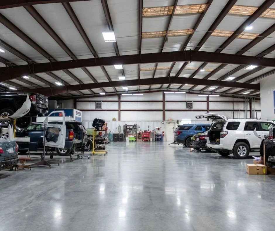 Automotive repair shop with cars, tools, and equipment inside a spacious warehouse with a high ceiling.