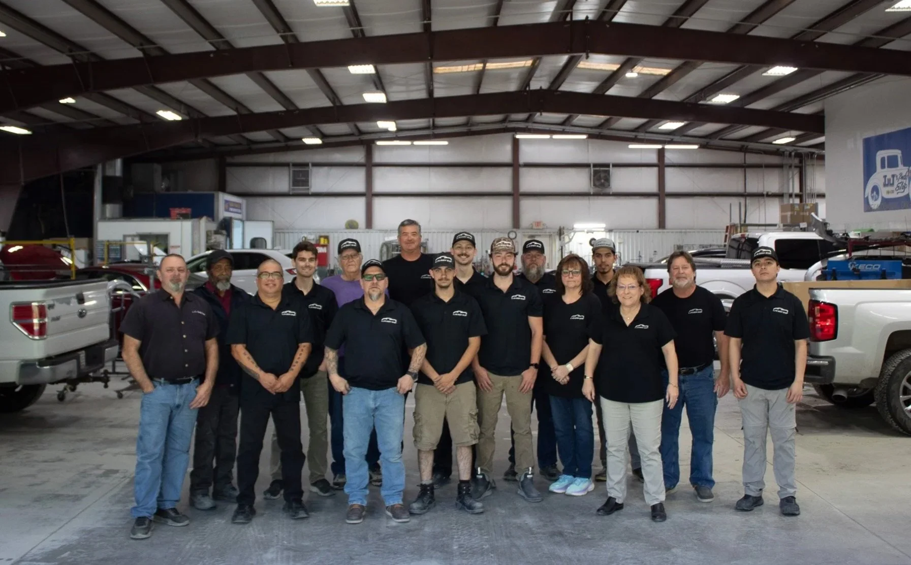 Group of 16 employees standing inside an auto repair shop, with trucks and equipment in the background.
