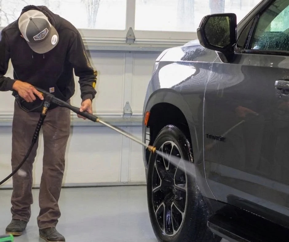 A man using a pressure washer to clean a gray car inside a garage.