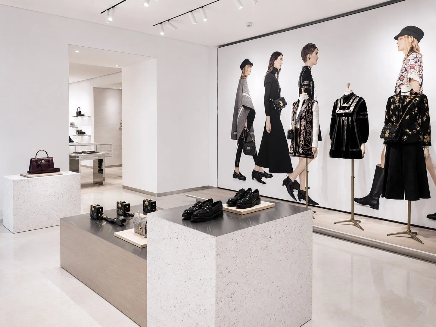 Vitrine d'une boutique de vêtements et accessoires avec mannequins en vitrine portant des vêtements noirs et colorés, et une table avec des chaussures et sacs à main.