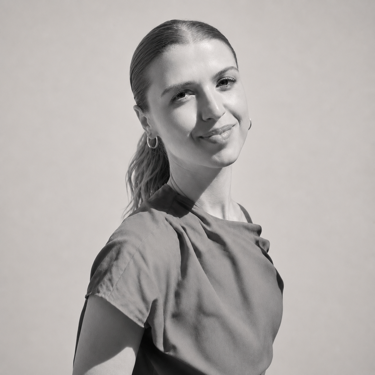 Portrait en noir et blanc d'une femme souriante avec des boucles d'oreilles en cercle, portant un haut léger et regardant vers la caméra.
