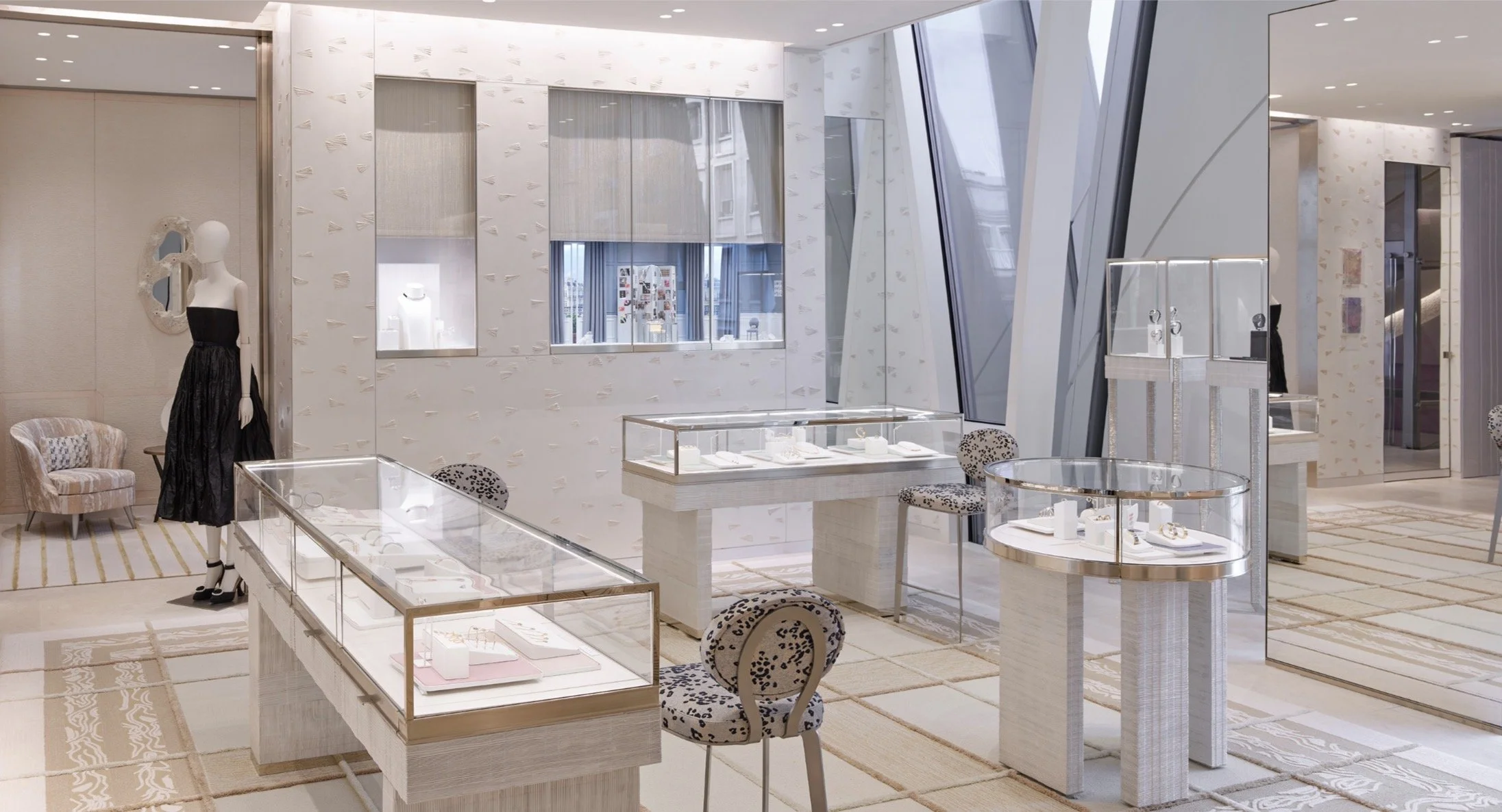 Une boutique de bijoux élégante avec des vitrines en verre contenant des bijoux fins, des meubles en blanc et des décorations modernes, un mannequin avec une robe noire, et des sièges à motif animal pour les clients.