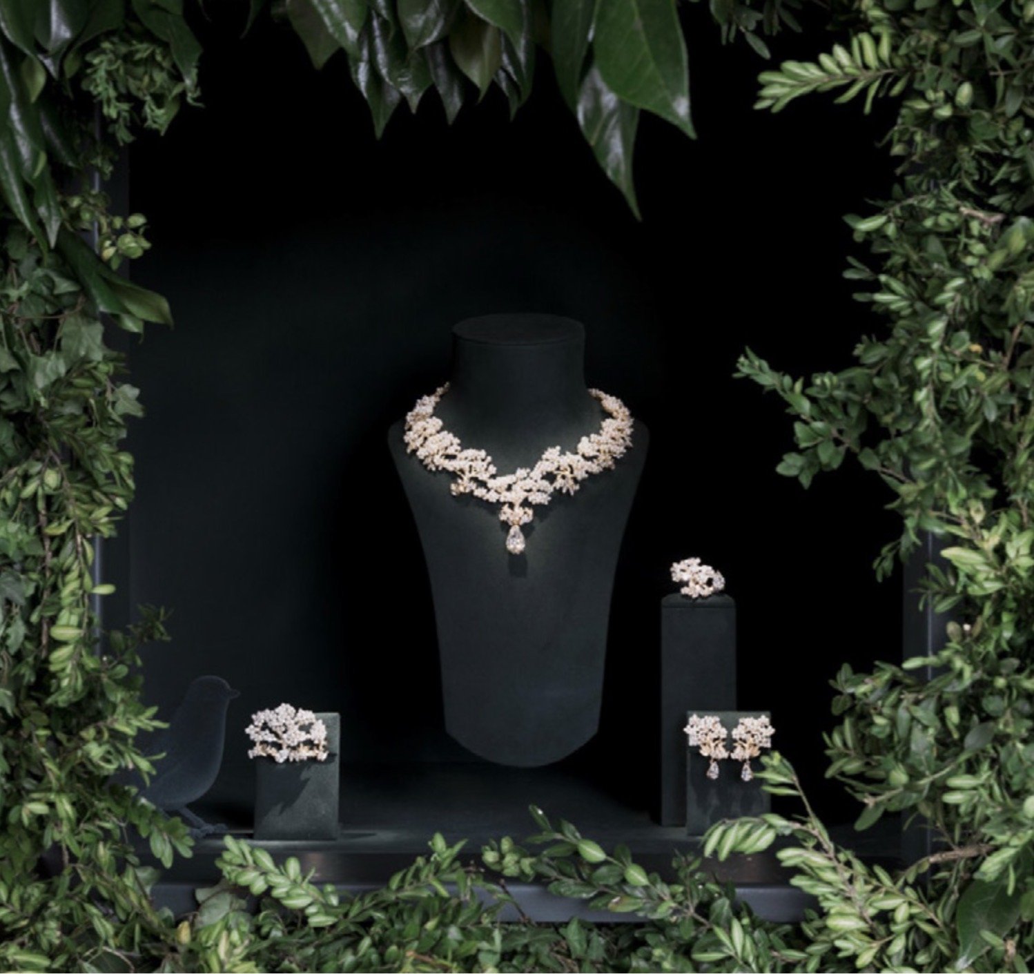 Vitrine présentant des bijoux, notamment un collier, des boucles d'oreilles et un bracelet, entourée de verdure.