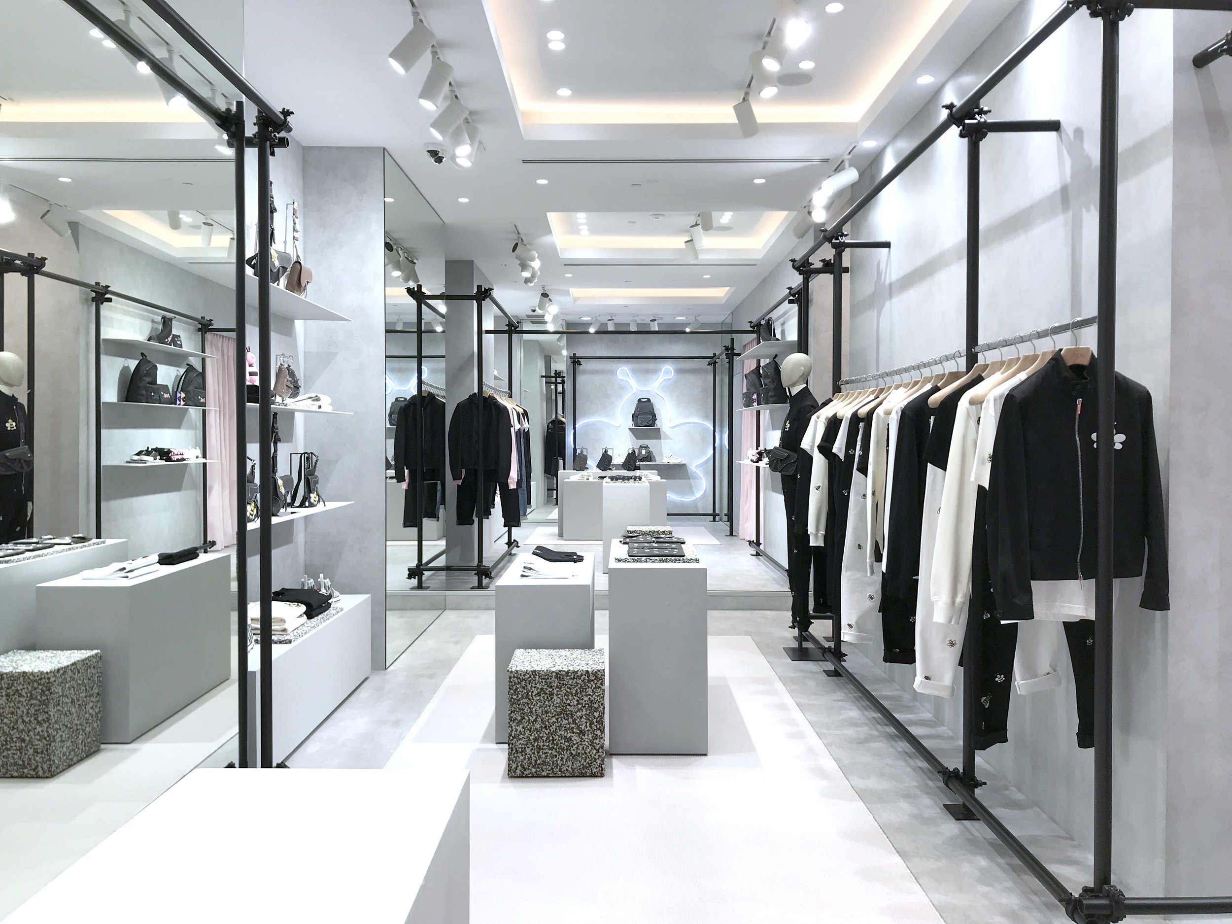 Vitrine d'une boutique de vêtements avec des vêtements suspendus et des sacs à main sur des étagères, intérieur moderne en blanc et gris.