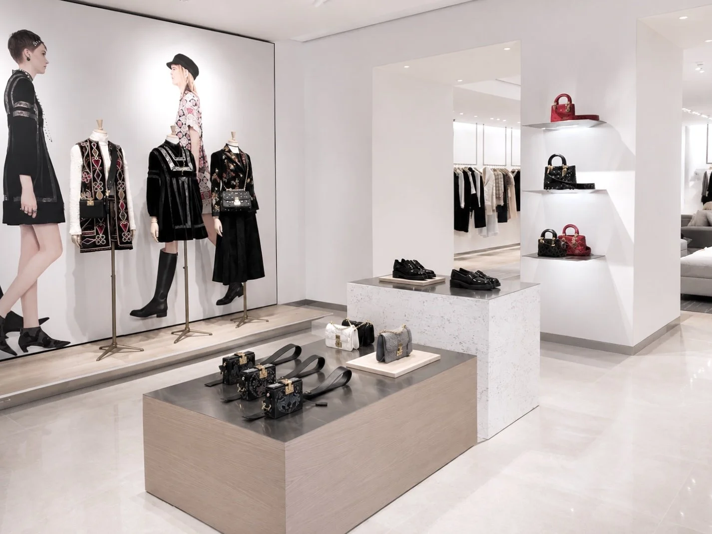 Intérieur d'une boutique de mode avec mannequins portant des vêtements, étagères avec des sacs à main, et une vitrine présentant des chaussures.