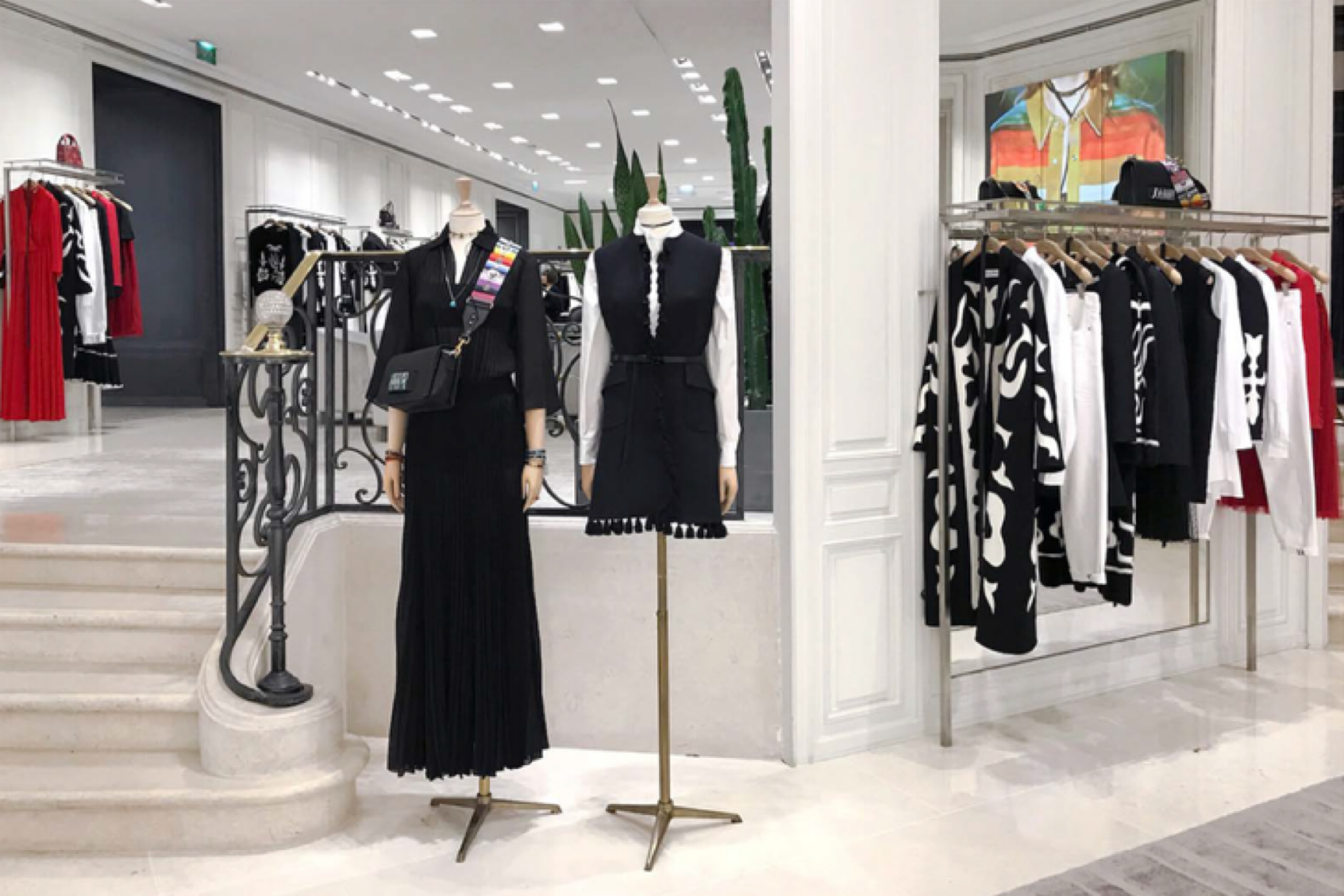 Vitrine d'un magasin de vêtements avec mannequins portant des tenues noires et blanches, et étagères avec des vêtements noir, blanc et rouge.