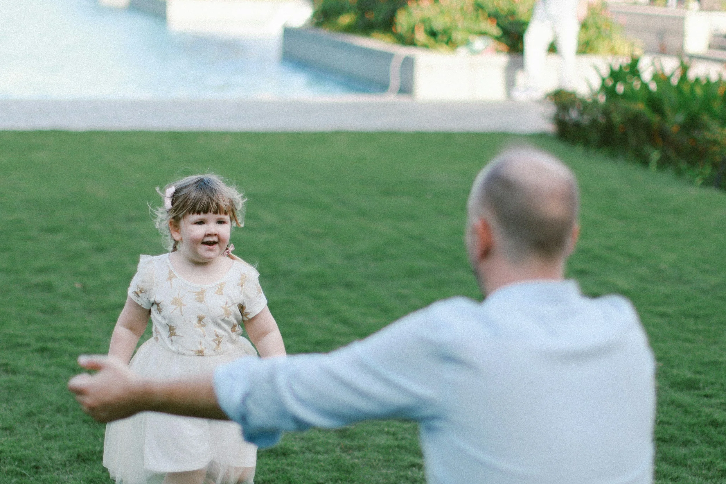 young girl standing on grass and smiling while running towards man with outstretched arms