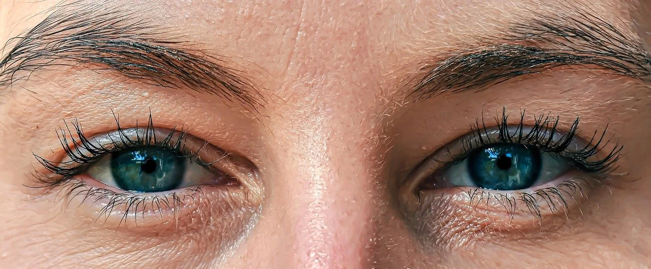 Close-up of a person's blue eyes with long eyelashes and detailed skin texture.