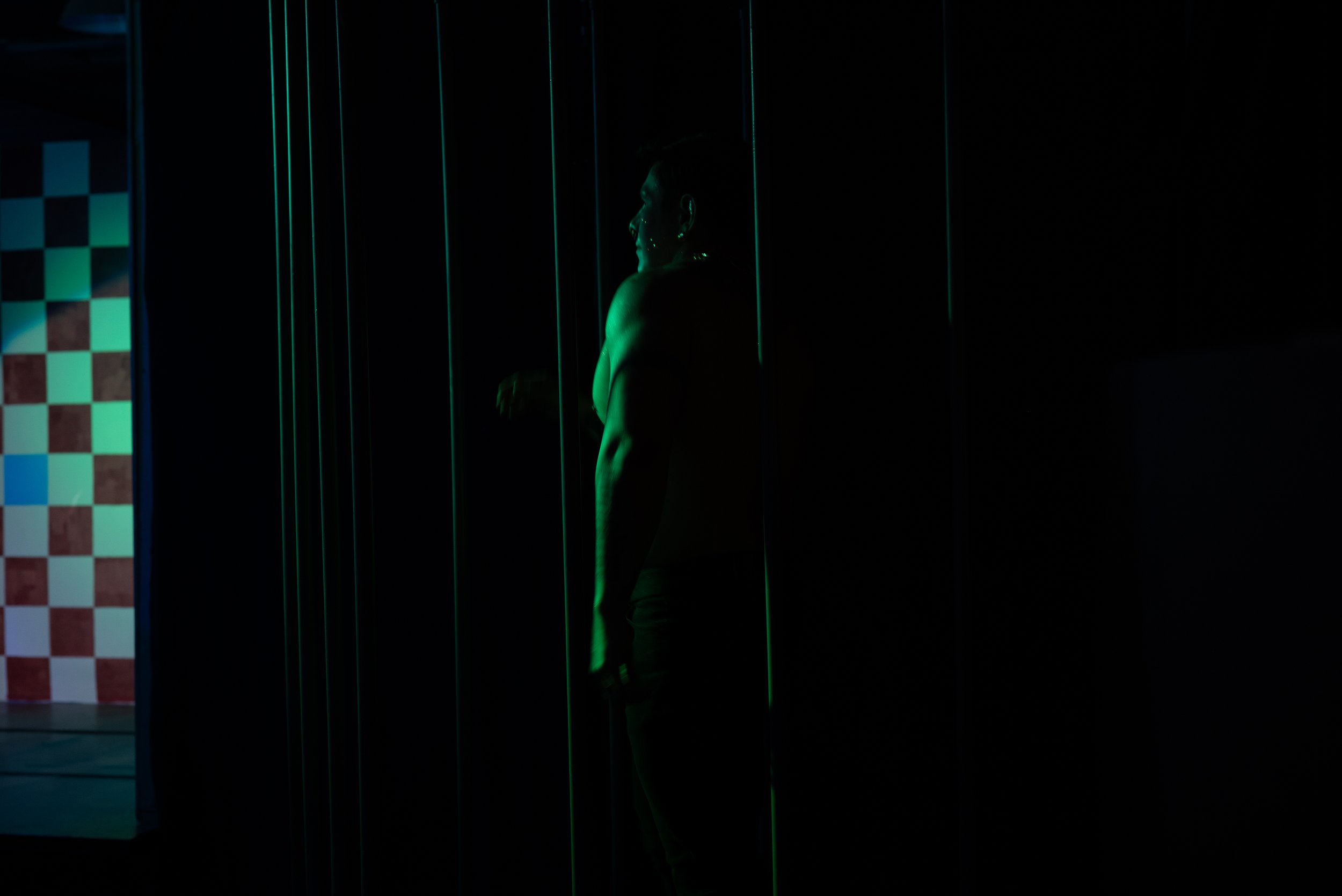 A person standing in a dark room next to black vertical panels, with neon green lighting highlighting their outline.