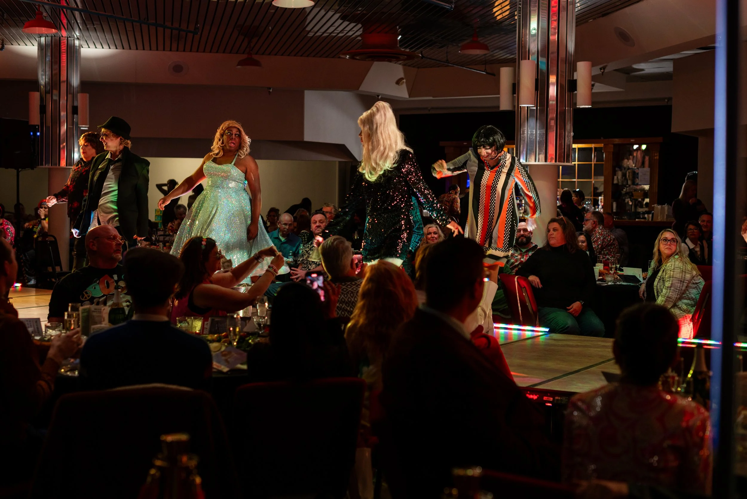 People performing on stage at a lively event, with an audience seated at tables watching the show.