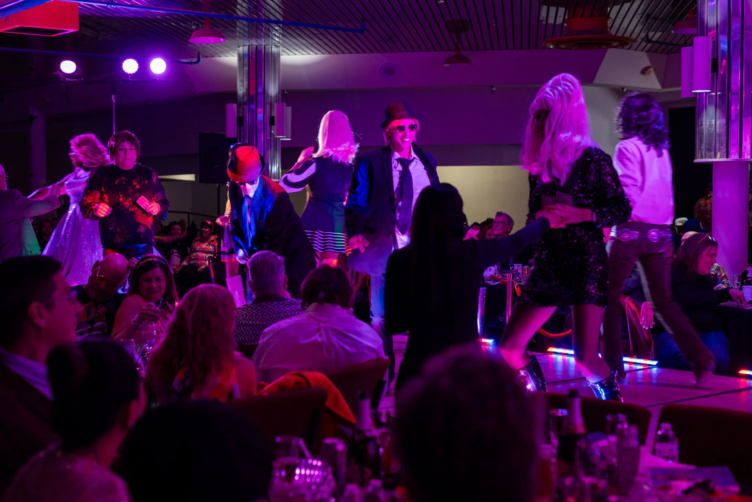 People dancing on a stage with purple and pink lighting during a celebration or party.
