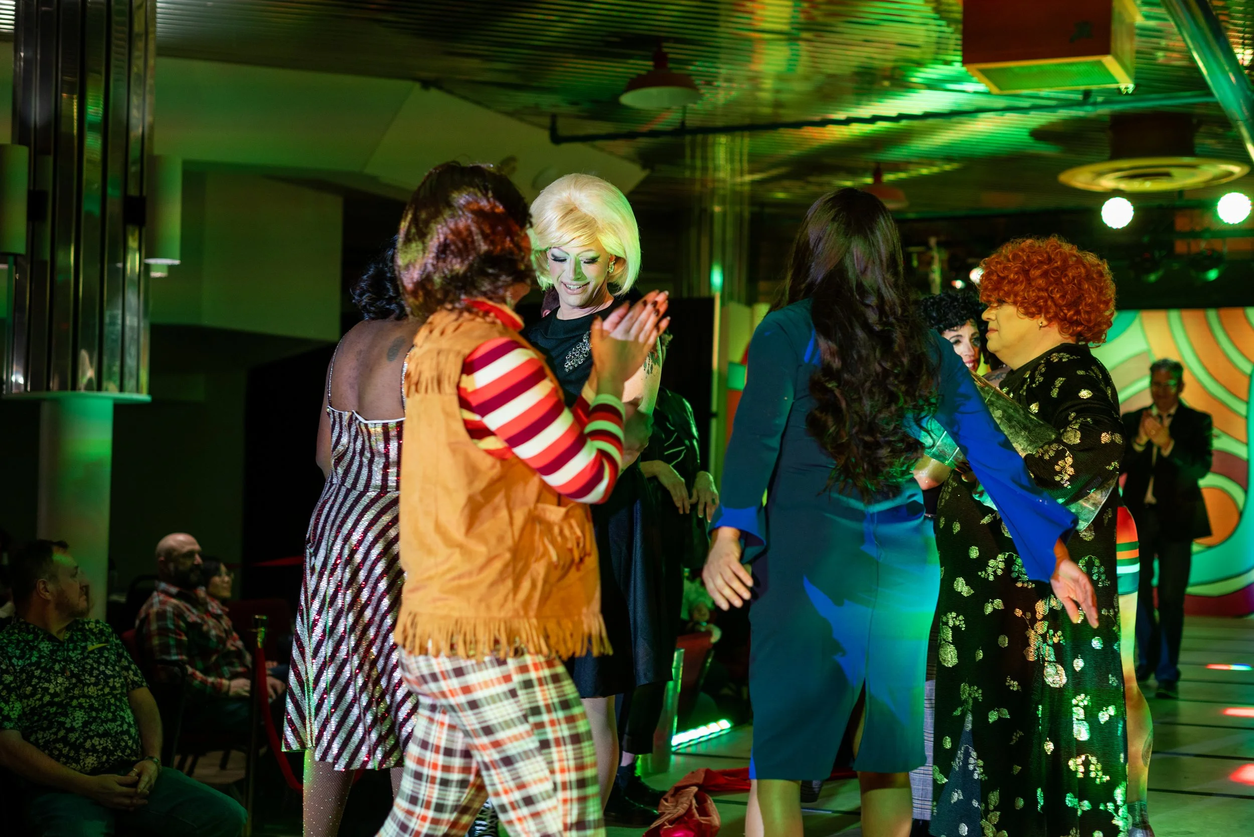People dressed in colorful costumes dancing and celebrating at a party or event with green lighting and a lively atmosphere.