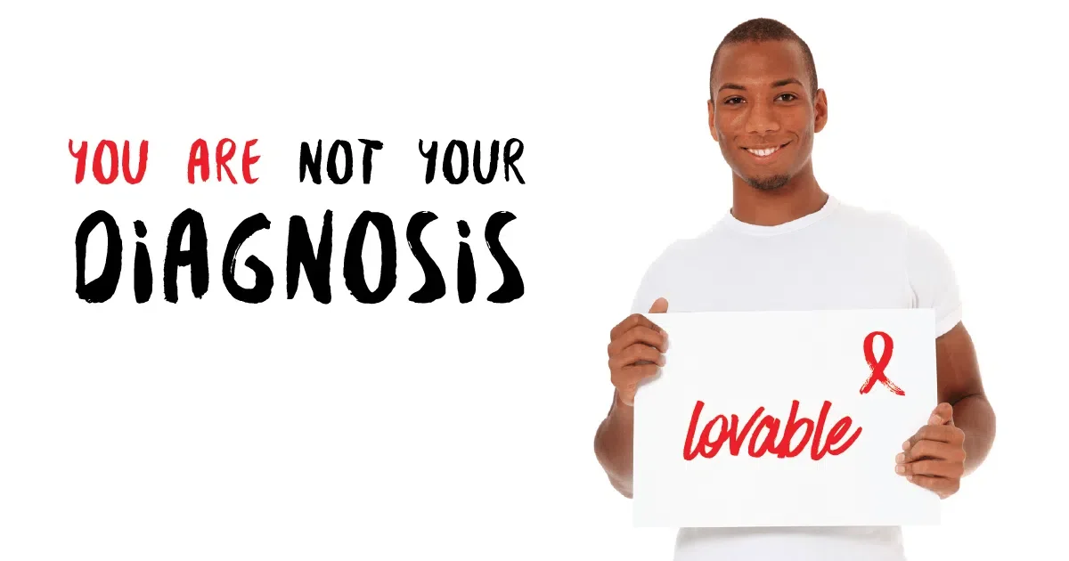 A smiling person holding a sign that says 'lovable' with a red ribbon symbol, and a message that says 'You are not your diagnosis' in black and red text.