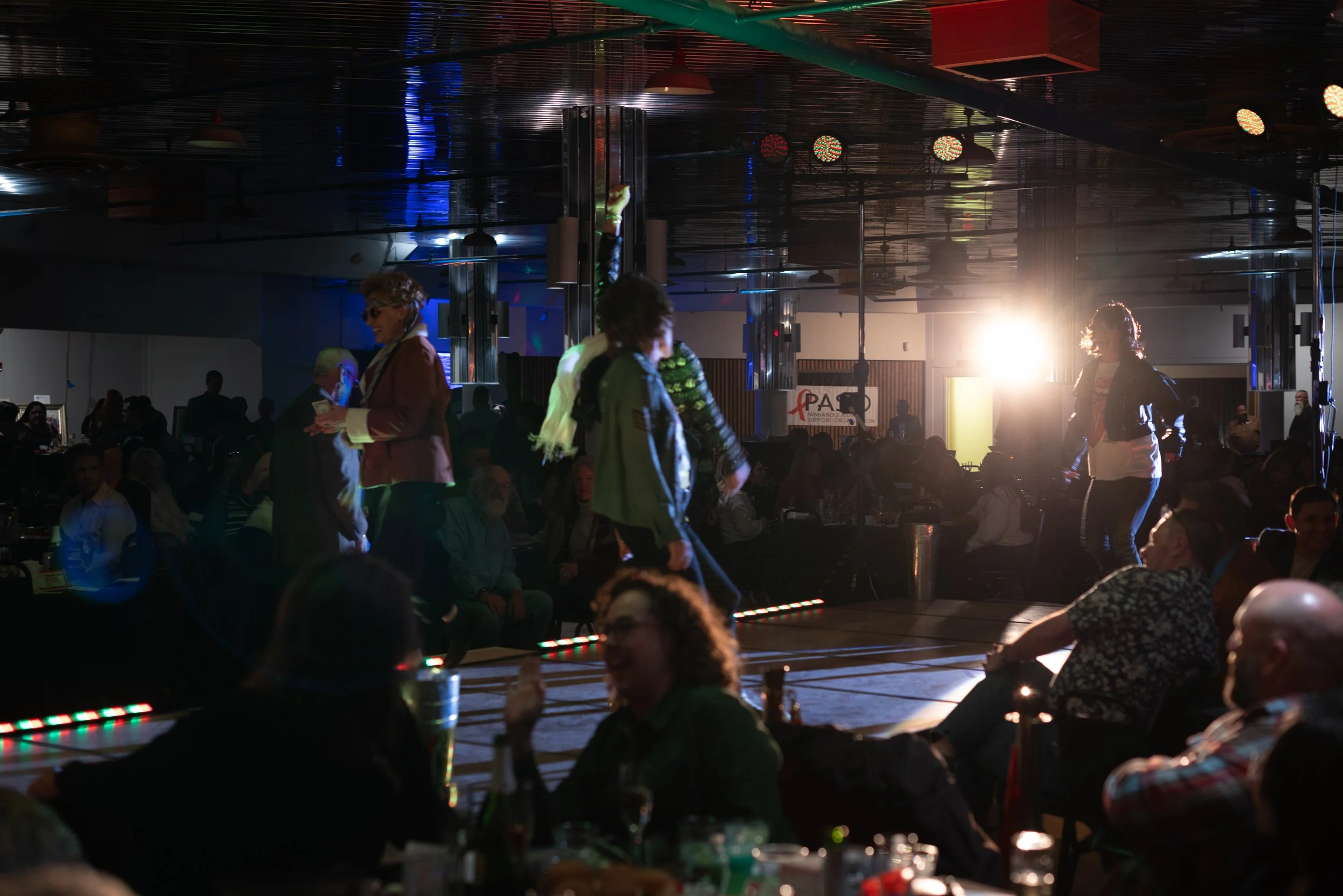 People watching a stage performance in a dimly lit venue with bright stage lights and a large crowd.